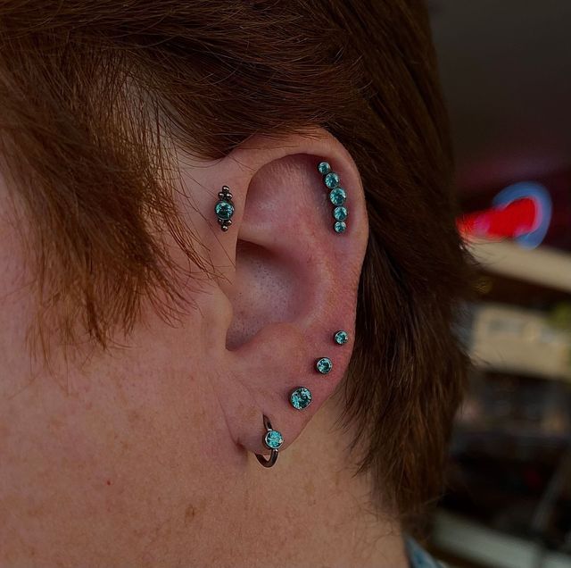 Close-up of an ear with multiple turquoise piercings and short brown hair