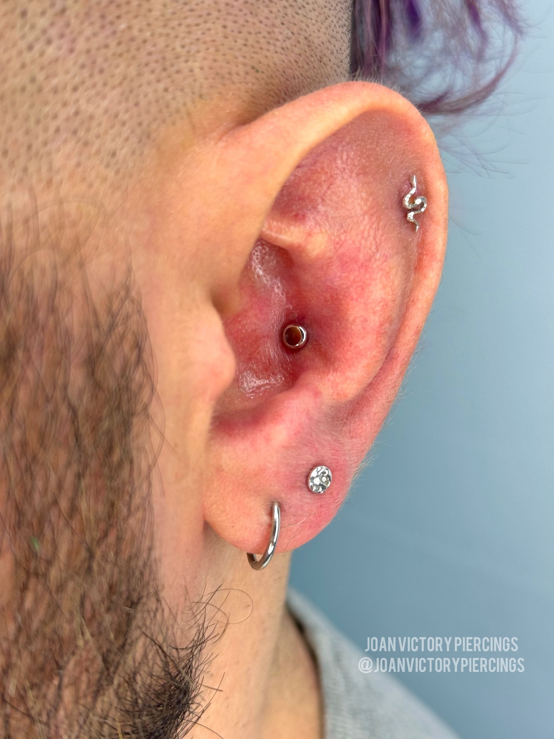 Close-up of an ear with multiple piercings, including a snake stud, a hoop, and a gem.