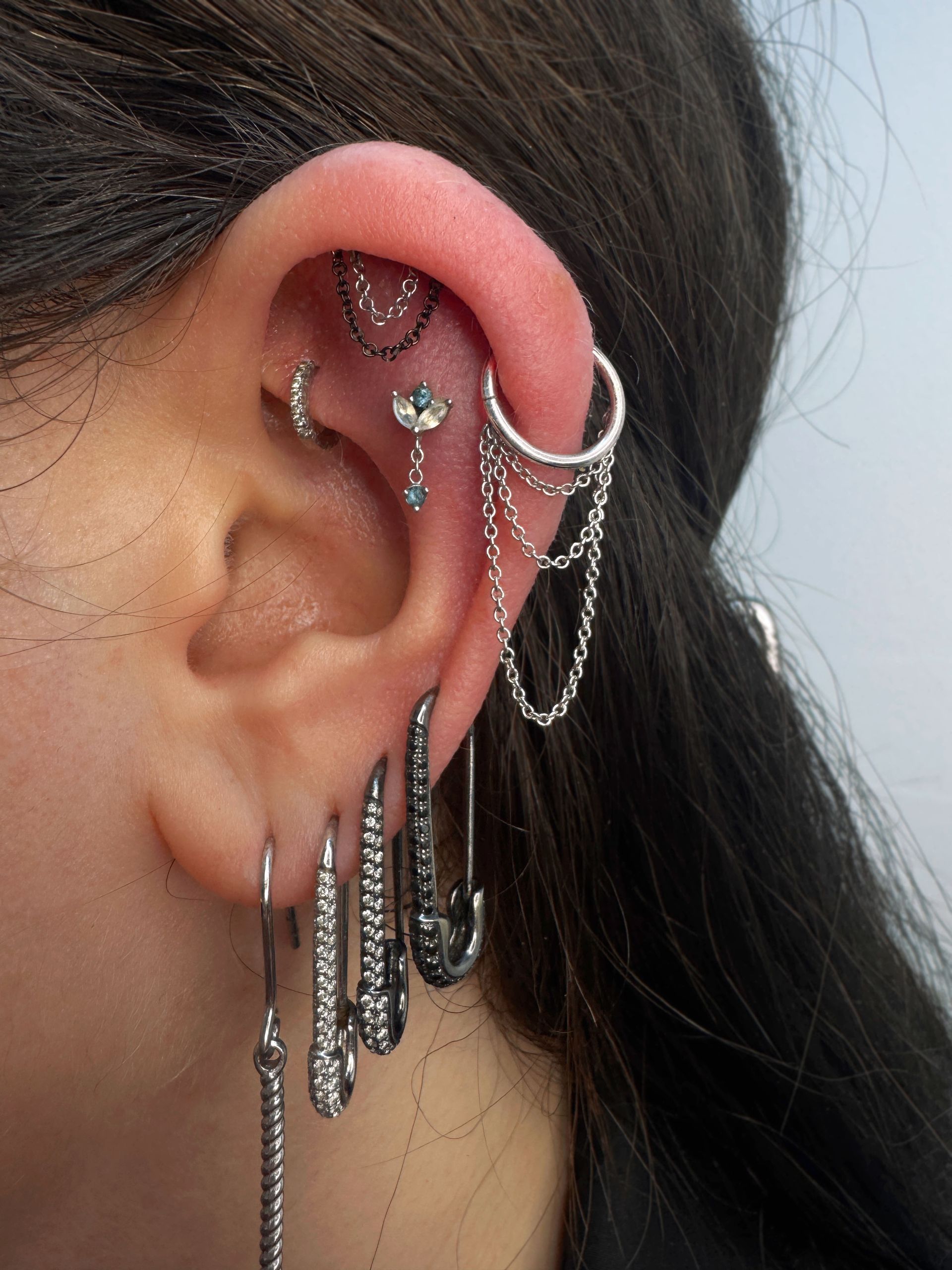 Close-up of ear with multiple piercings, including chain and safety pin earrings.