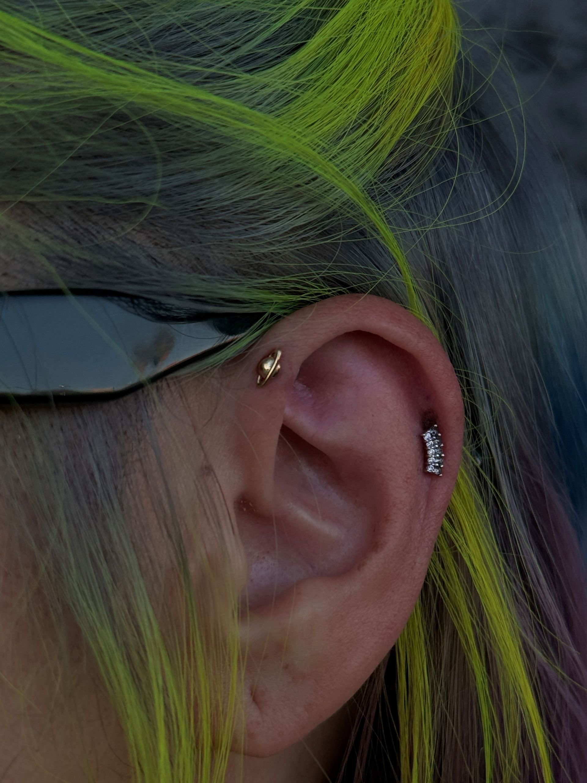 Ear with multiple piercings, yellow and green streaks in hair.