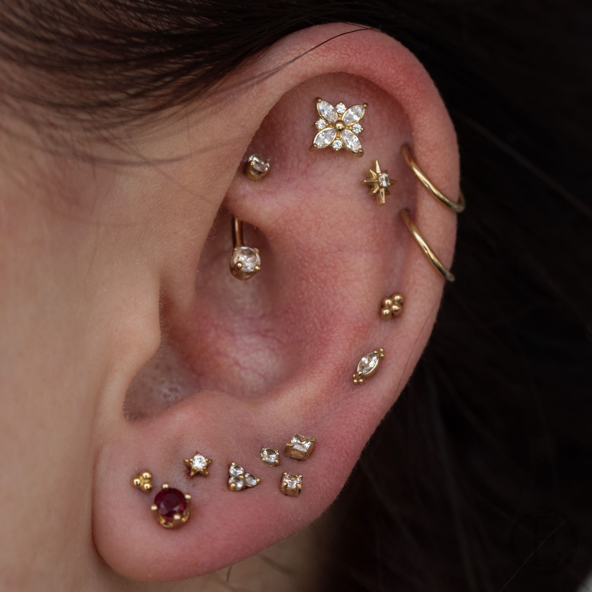 Close-up of an ear with multiple gold piercings, including studs, hoops, and a curved barbell.
