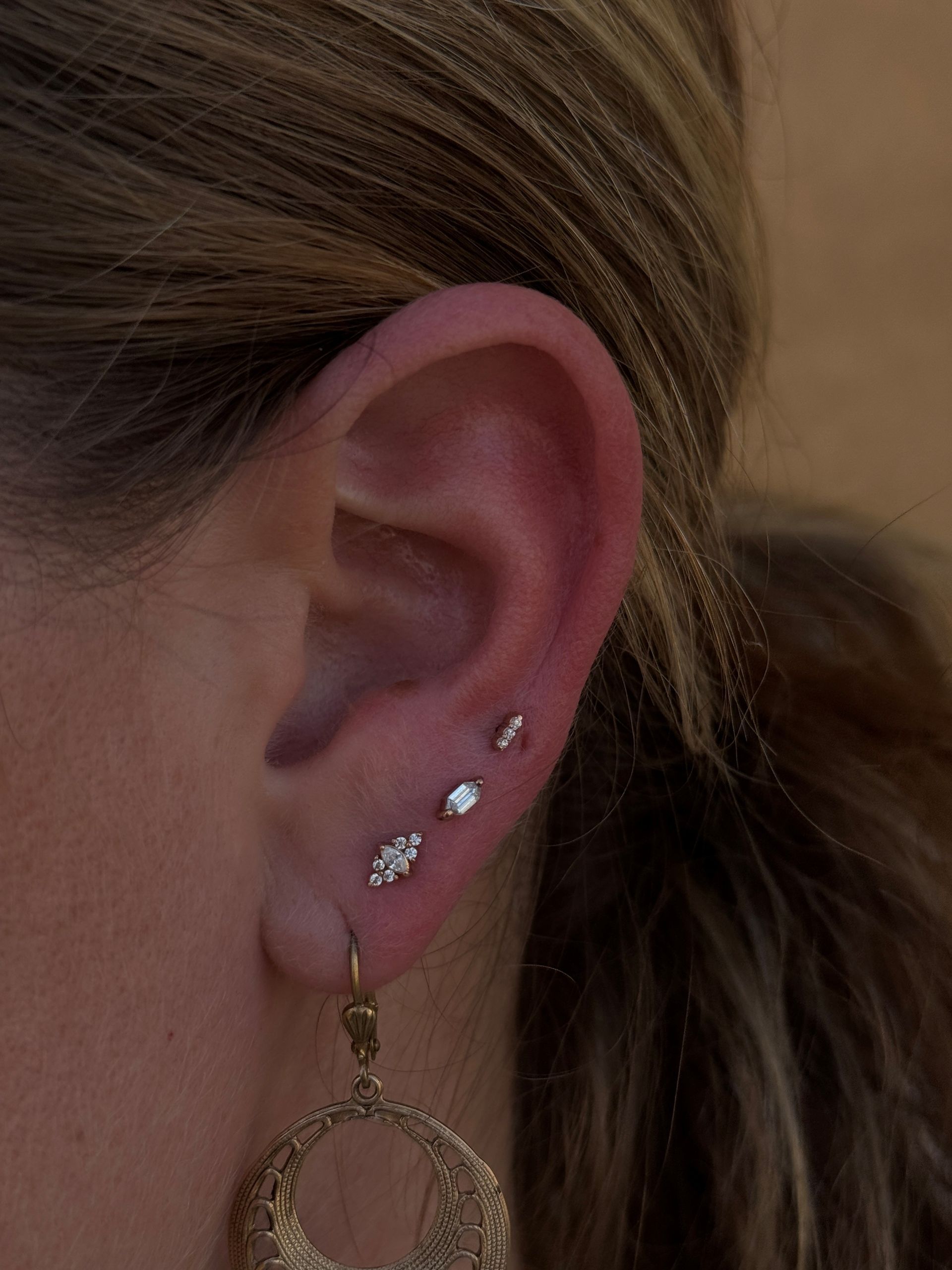 Close-up of ear with three small diamond stud earrings and a gold hoop earring hanging from the lobe.
