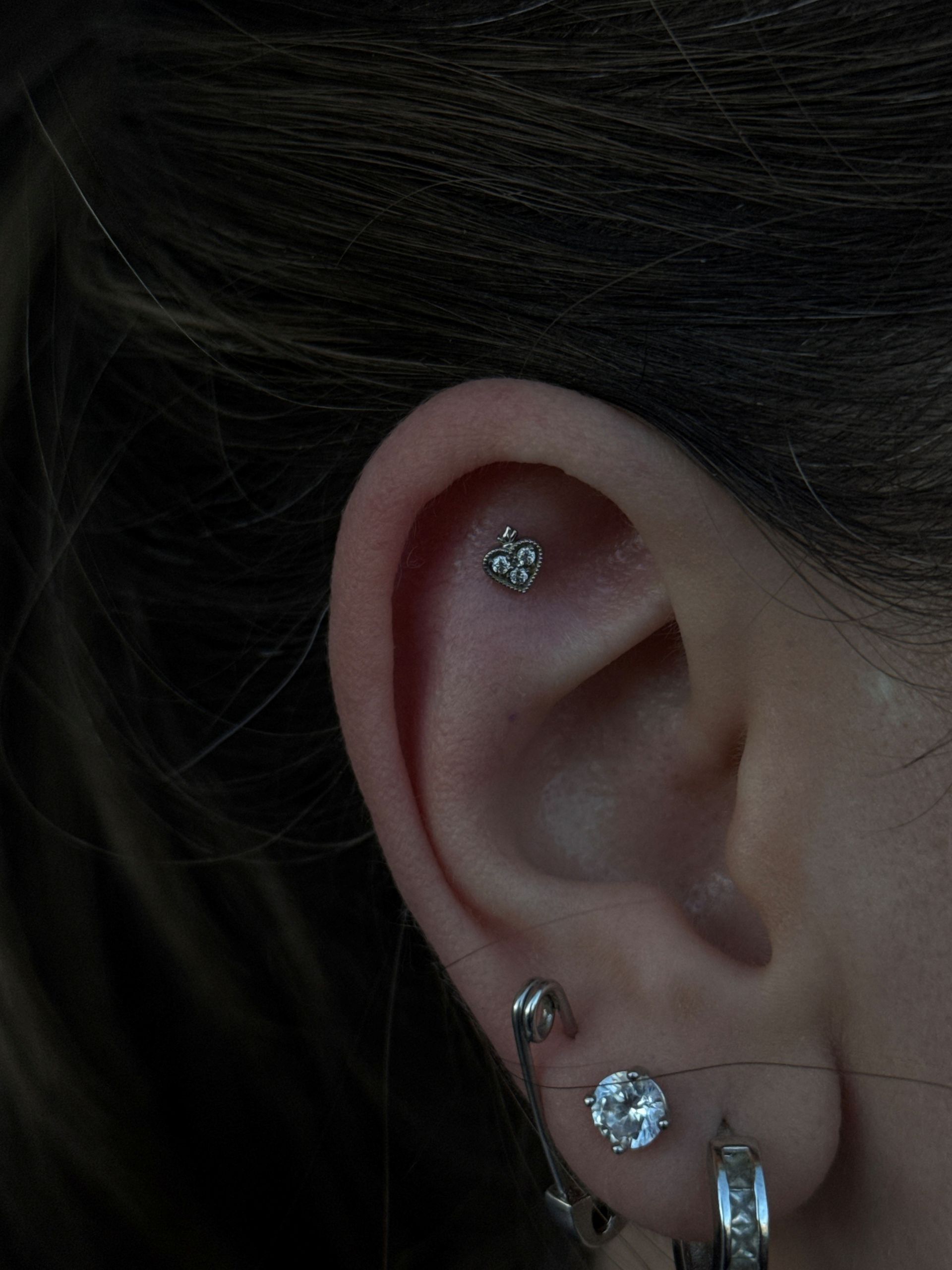 Ear with three piercings: a flower-shaped stud on the upper ear, a gem, and a hoop earring with gems.