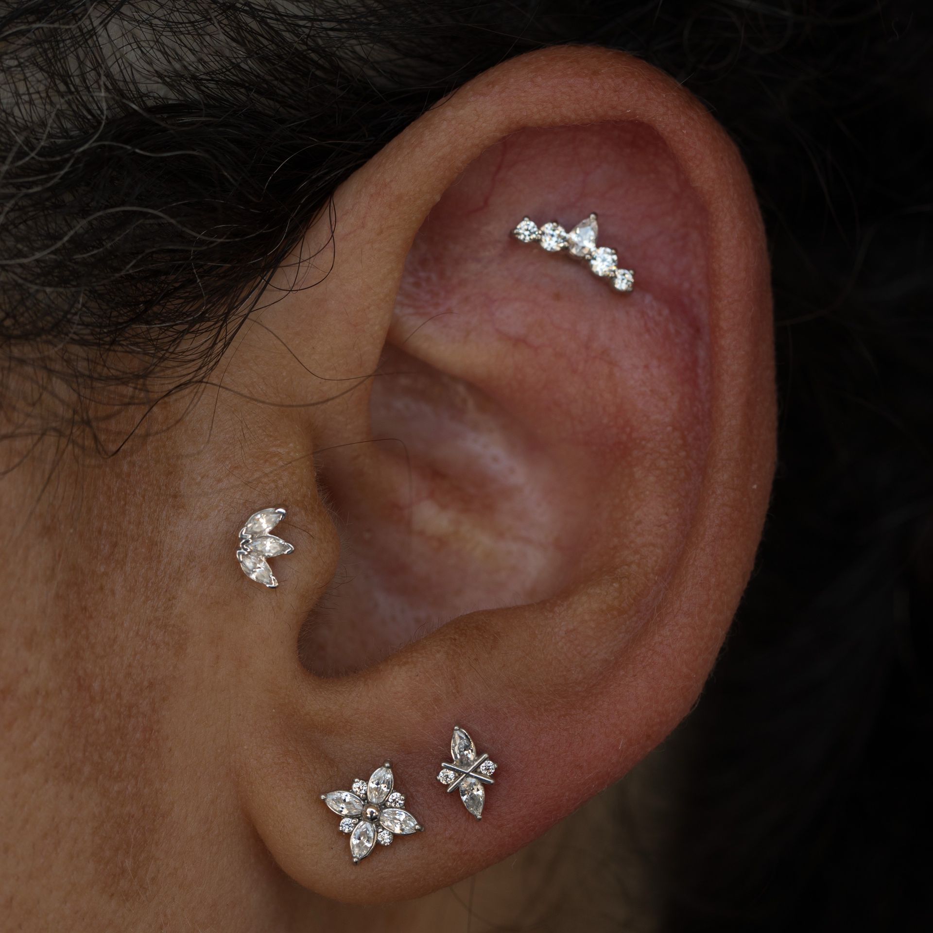 Close-up of an ear with four decorative piercings: curved bar, moon, flower, and lightning bolt.
