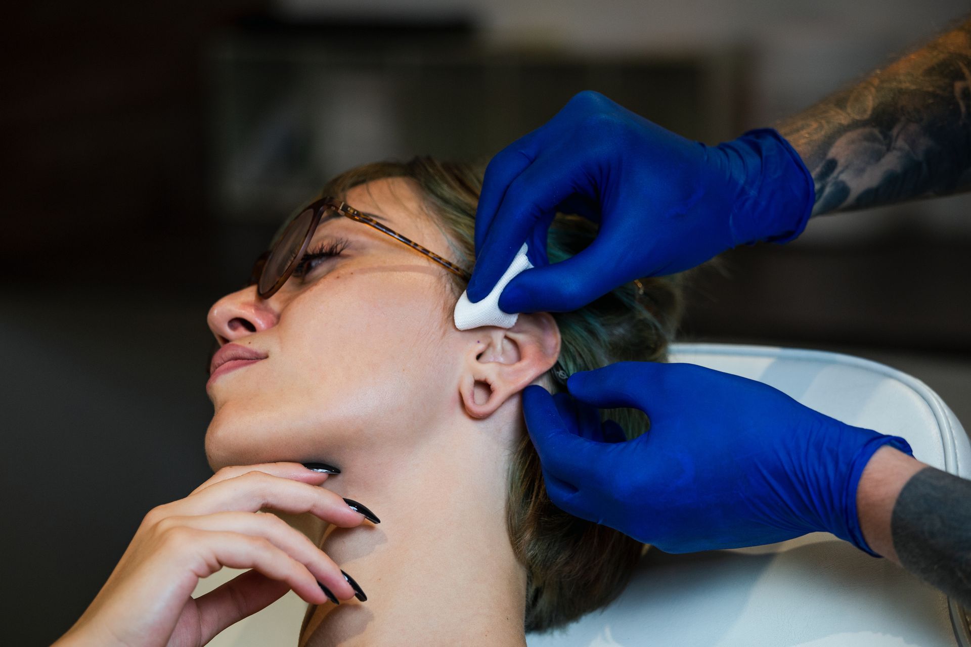 Woman with sunglasses having ear curation services in Manhattan, NY by man wearing blue gloves.