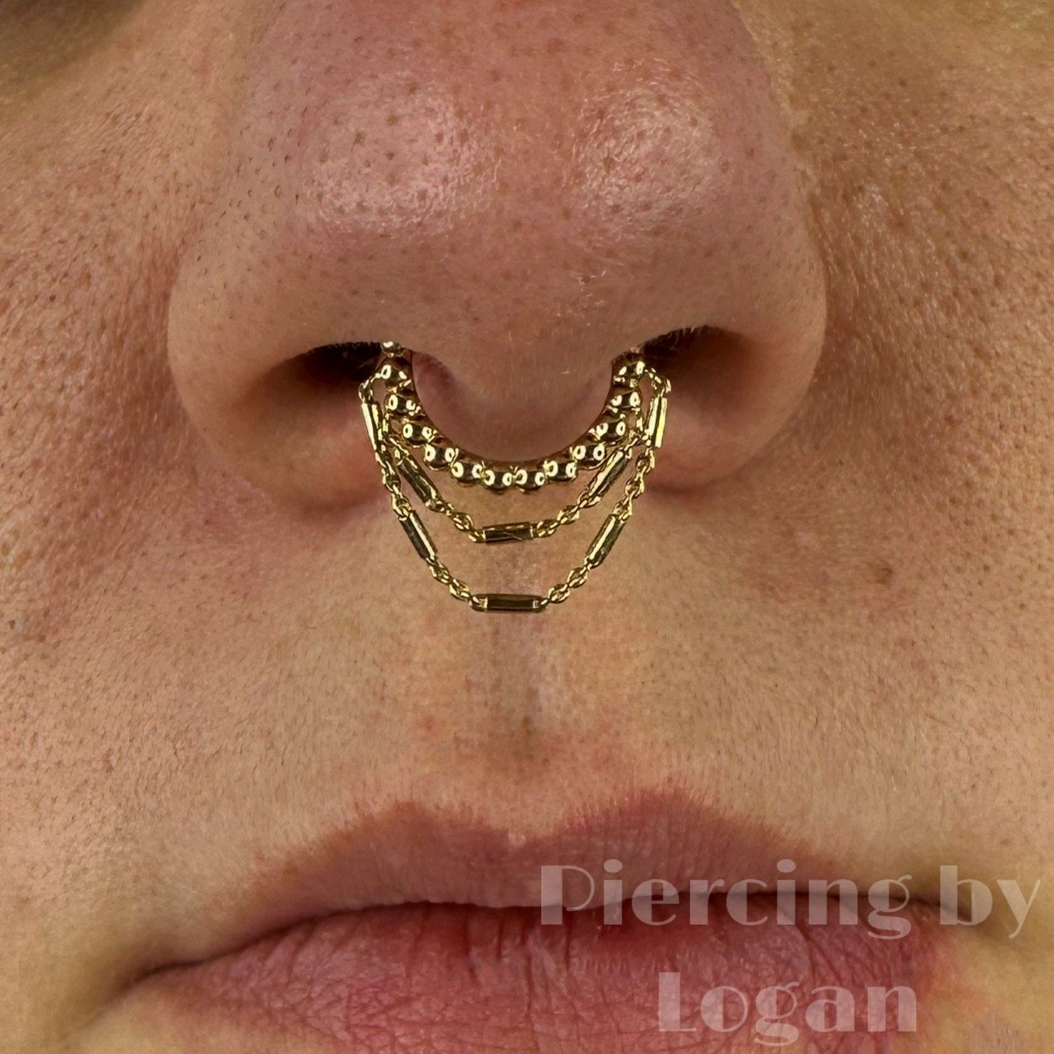 Close-up of a person's nose with a septum piercing featuring three gold chain dangles.