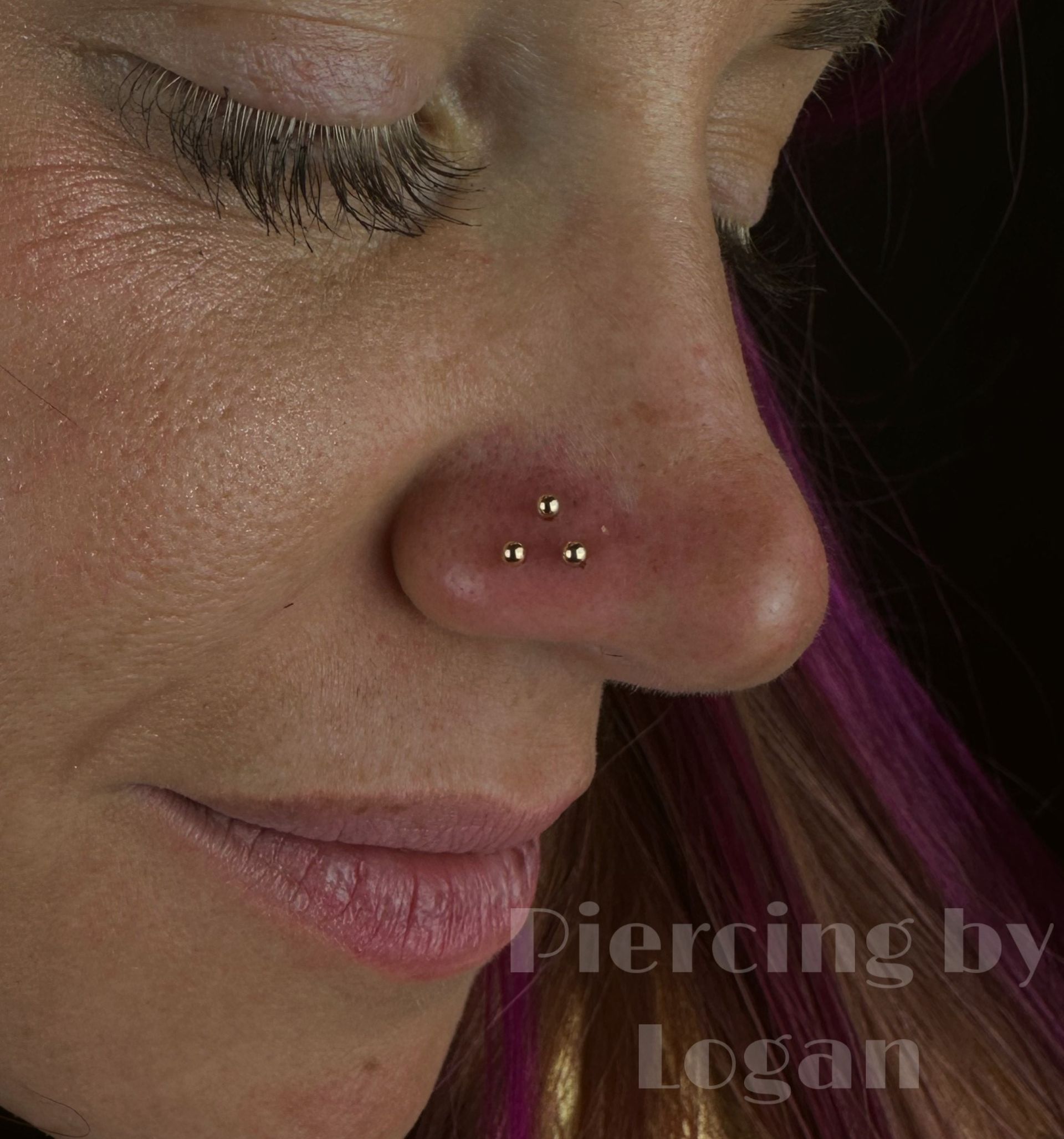 Close-up of a person's nose with three nose piercings. The skin is pale with pinkish areas, and the jewelry is silver.