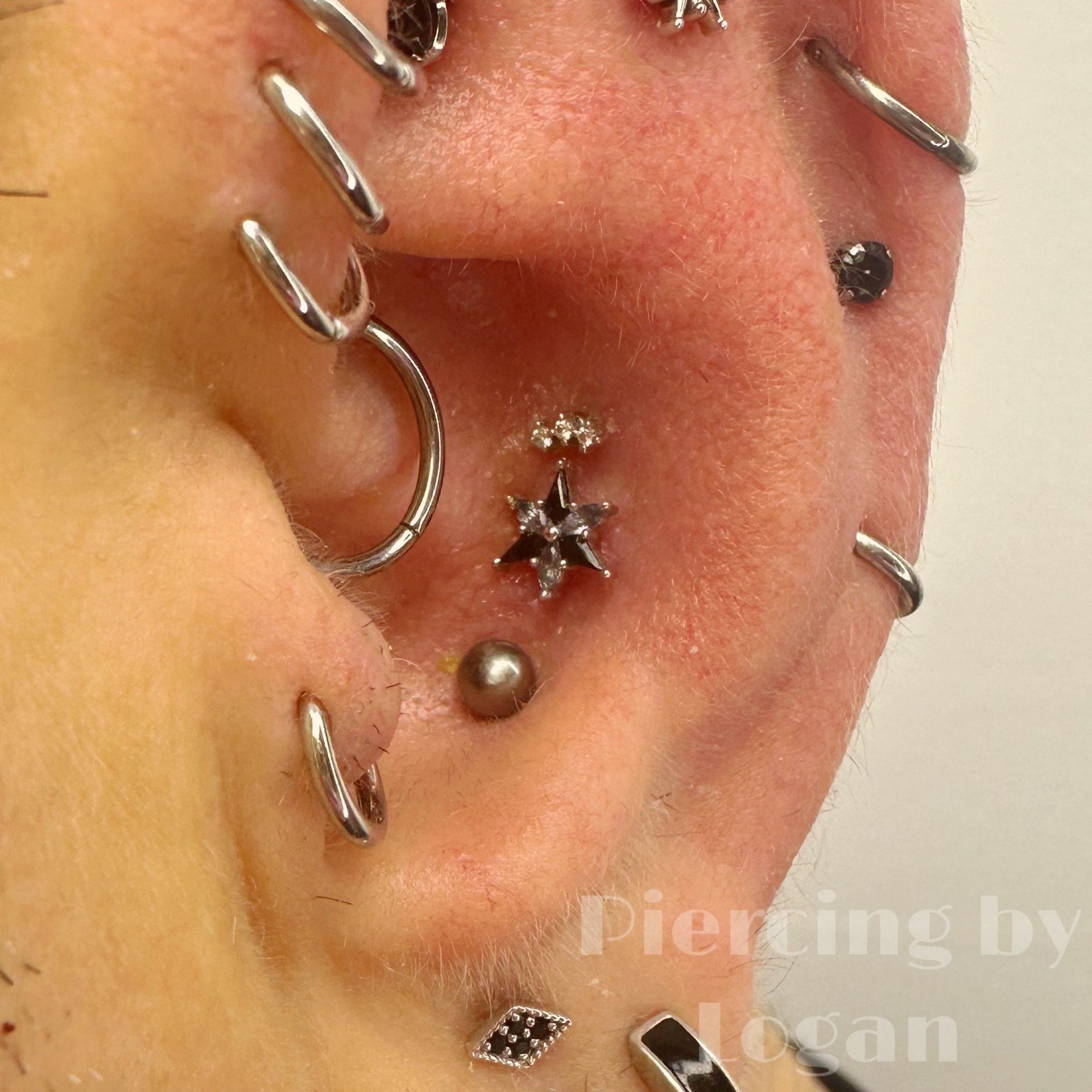 Close-up of an ear with multiple piercings, various silver and black jewelry.