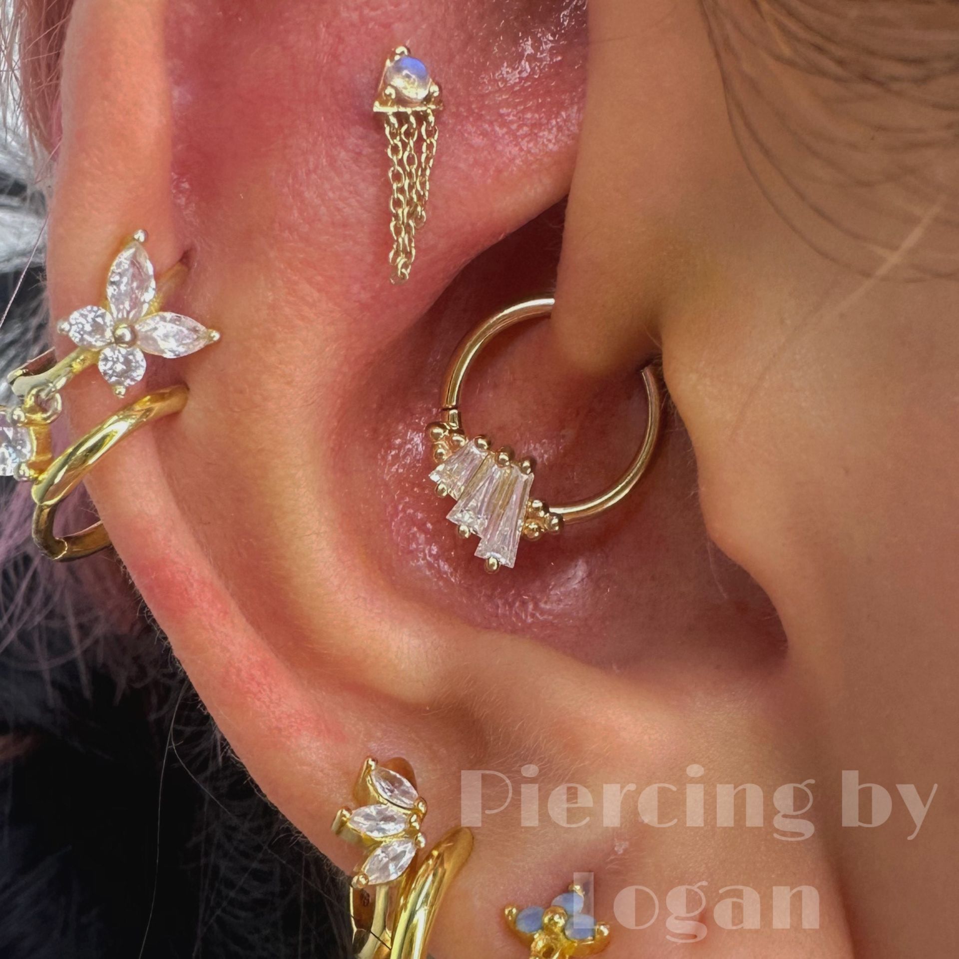 Close-up of ear piercings with gold jewelry, including a butterfly-shaped earring and a hoop with dangling gems.