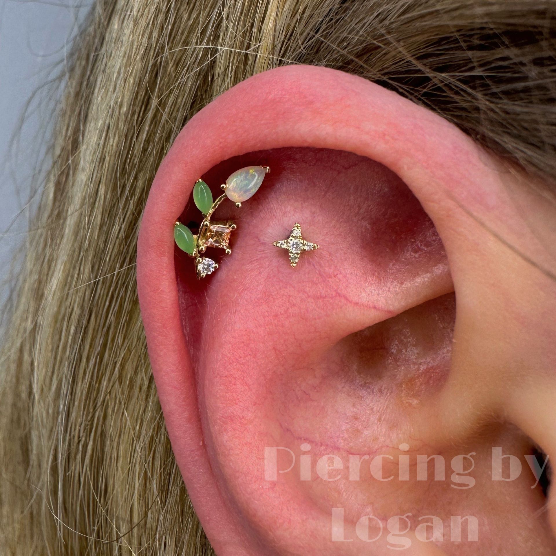 Close-up of ear with two gold and gemstone piercings: a floral cluster and a star.