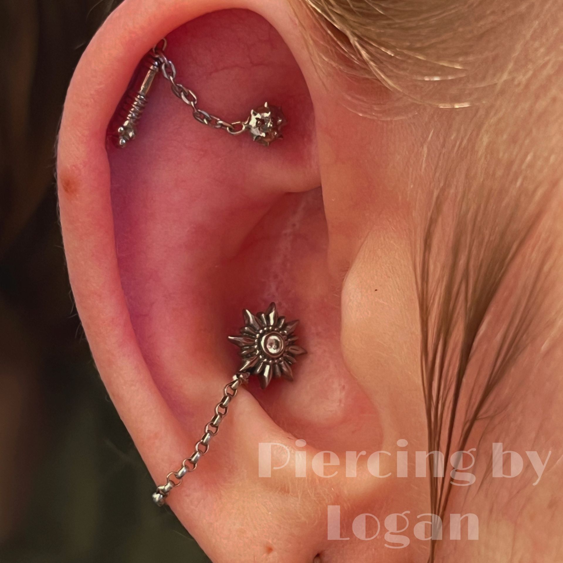 Ear with two piercings connected by a chain. The lower piercing features a sun-shaped charm.