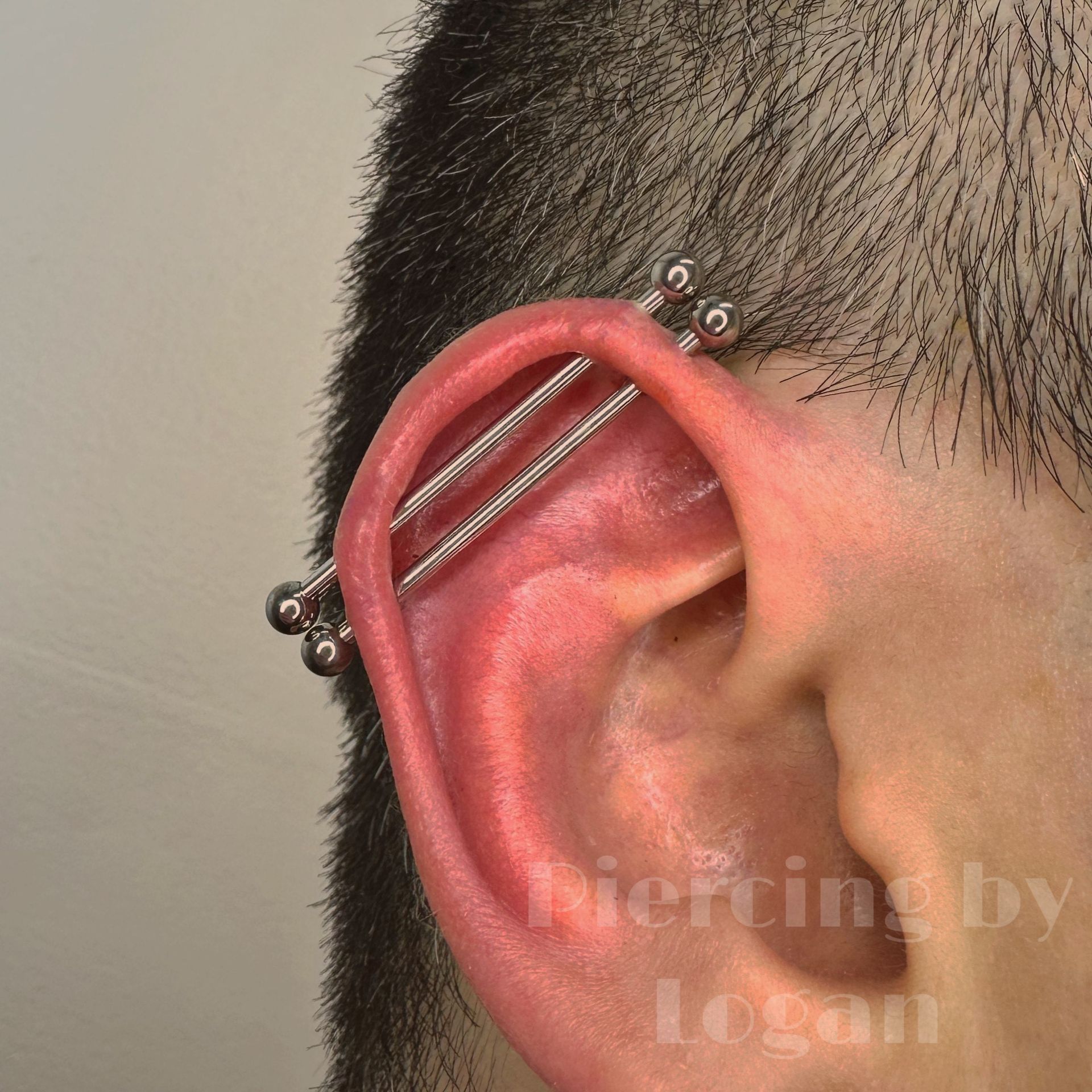 Close-up of an ear with a double industrial piercing. The ear is pink, with silver barbell jewelry.