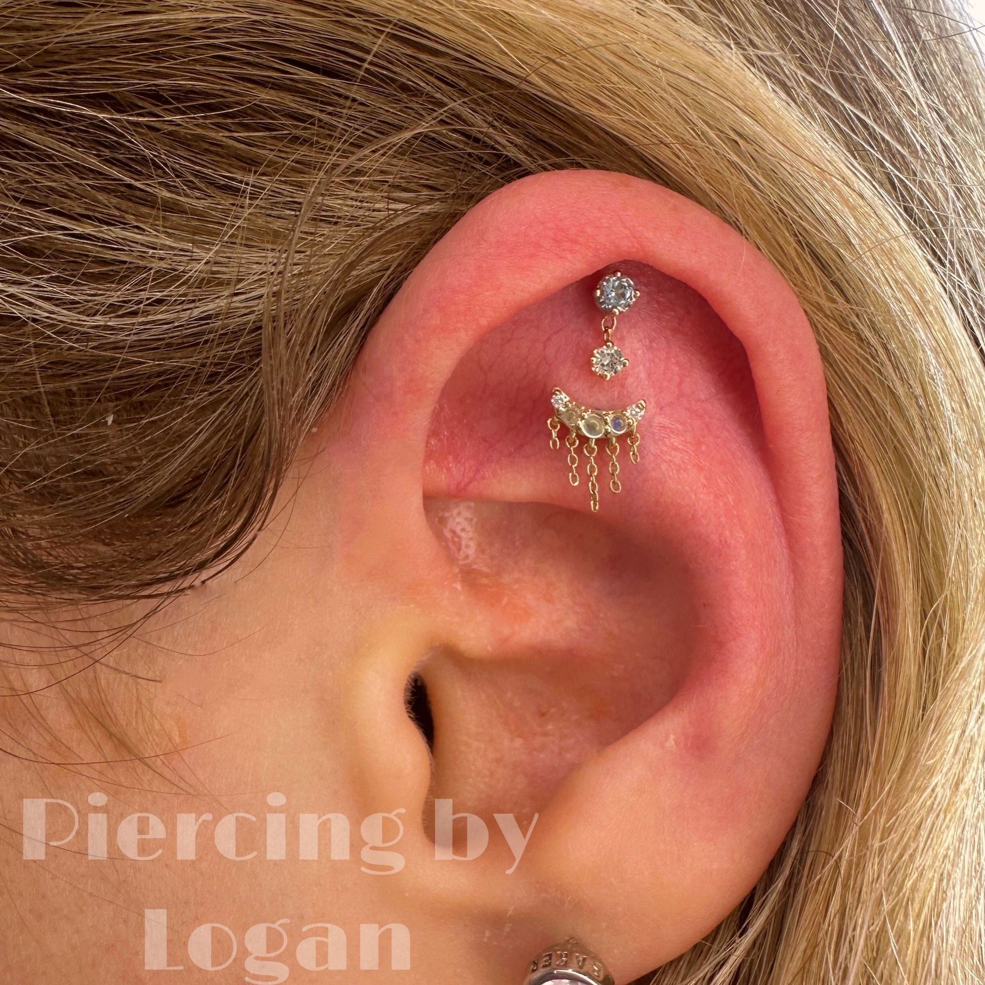 Ear with multiple piercings, including dangling gold and jewel-toned earrings.