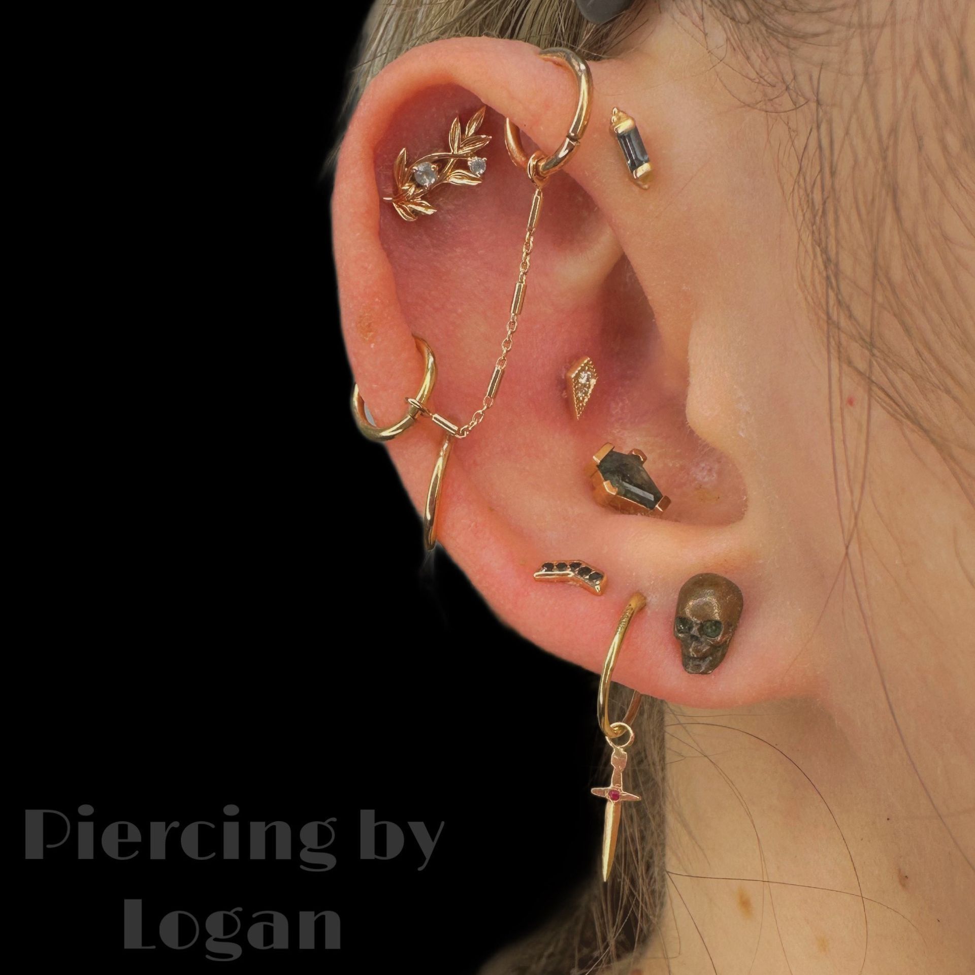 Ear with multiple gold piercings and jewelry, including rings, studs, and a chain.