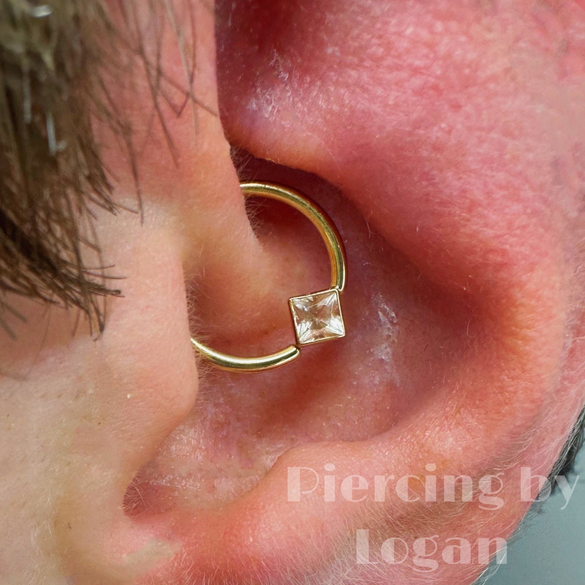 Gold hoop earring with square gem in a daith piercing.