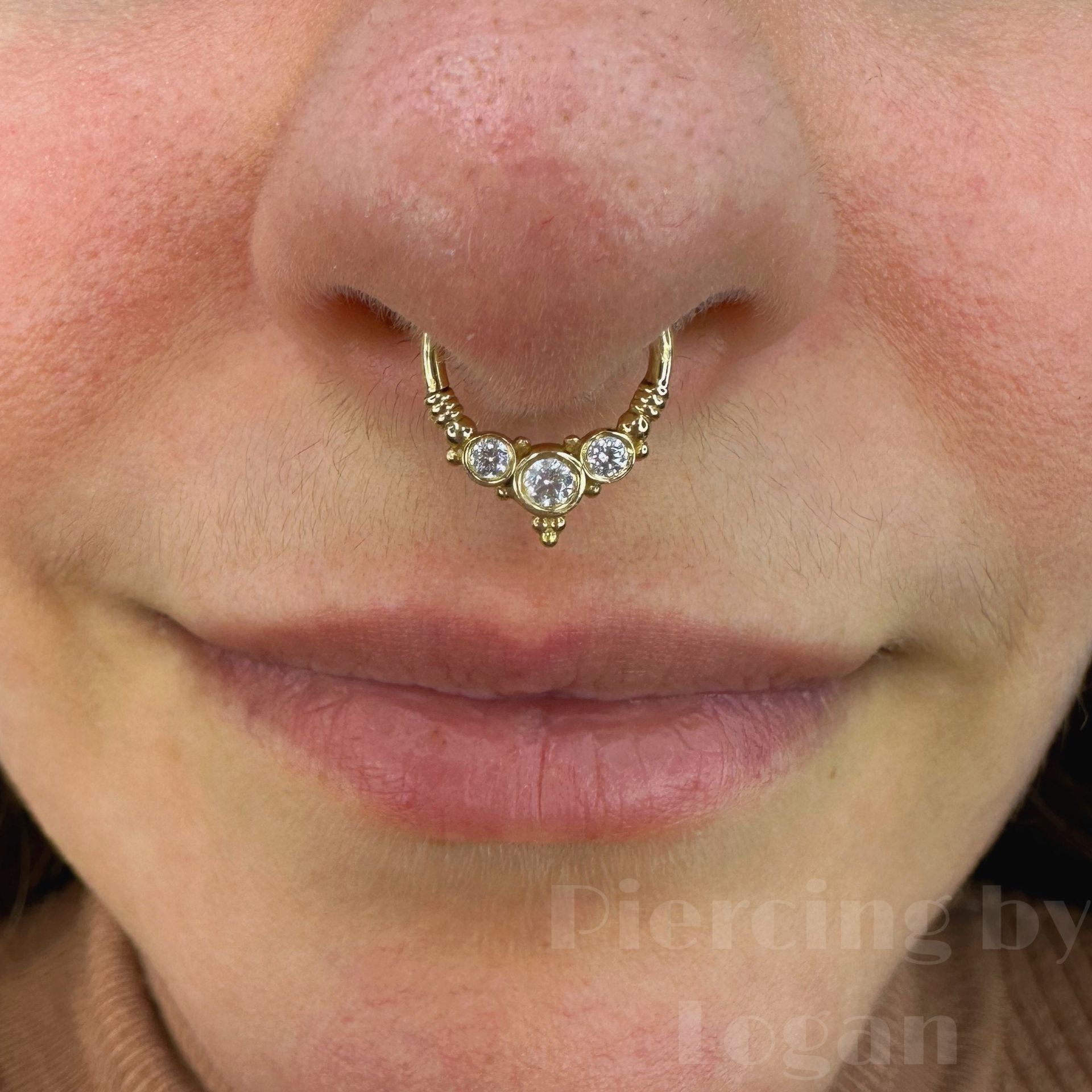 Close-up of a person's nose and mouth; they are wearing a gold septum piercing with three clear gemstones.