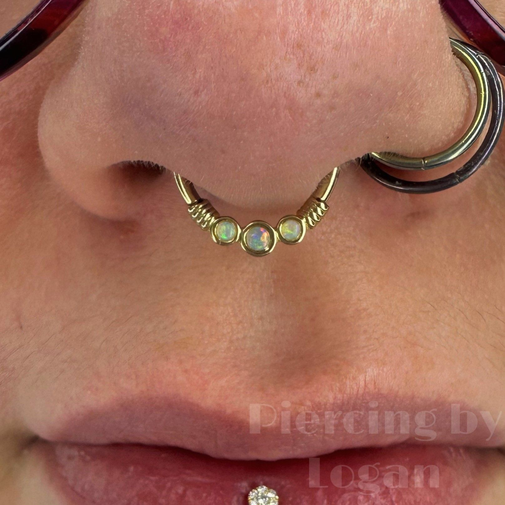 Close-up of a person's face with a septum piercing featuring three opals, and a lip piercing.