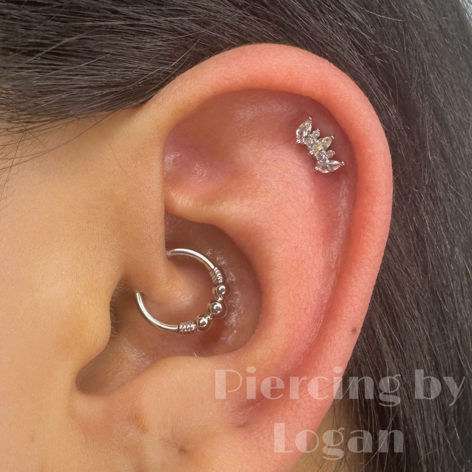 Close-up of an ear with a cartilage piercing and a daith piercing. The piercings are silver.