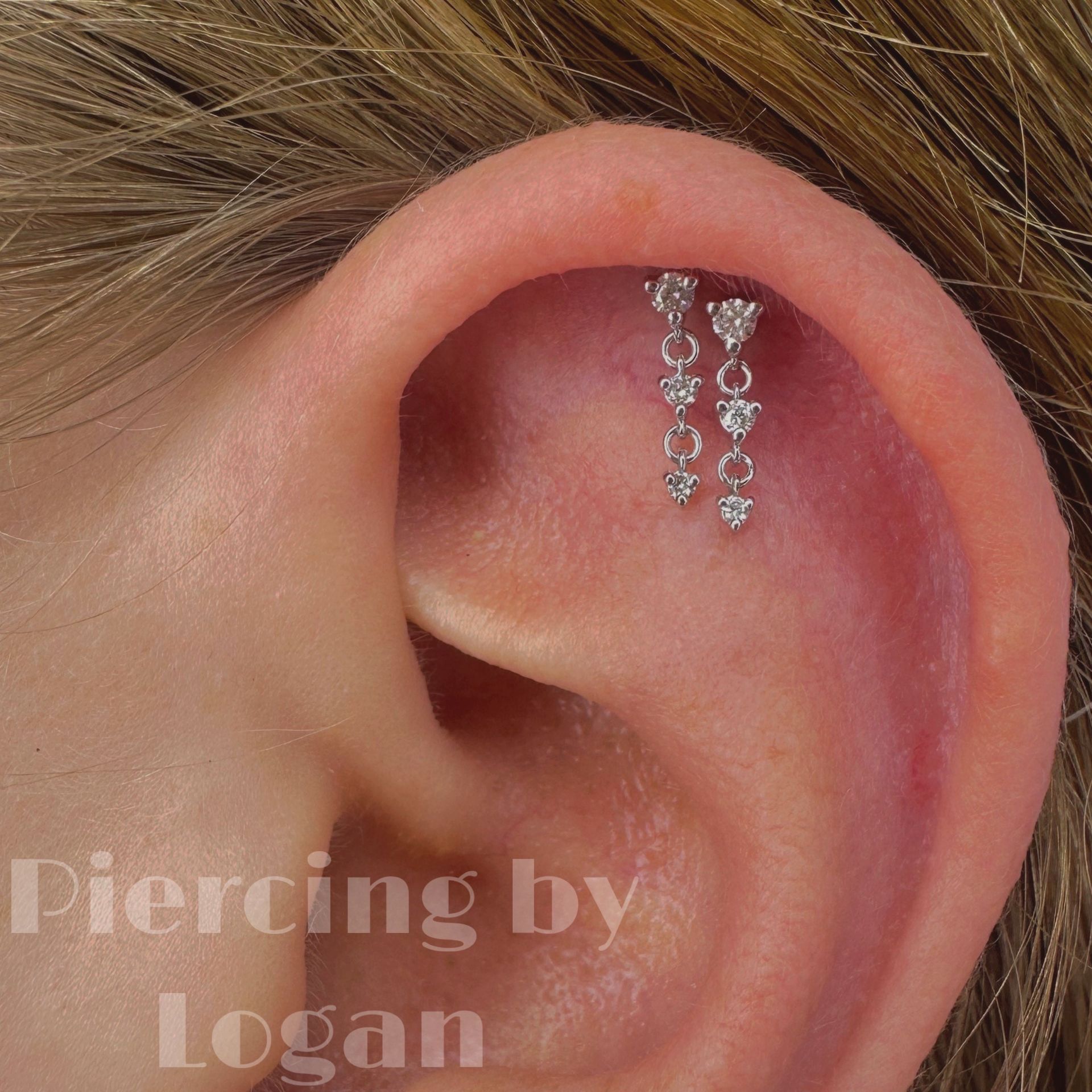 Ear with a double helix piercing and dangling charms. The ear is flesh-toned, and the jewelry is silver.
