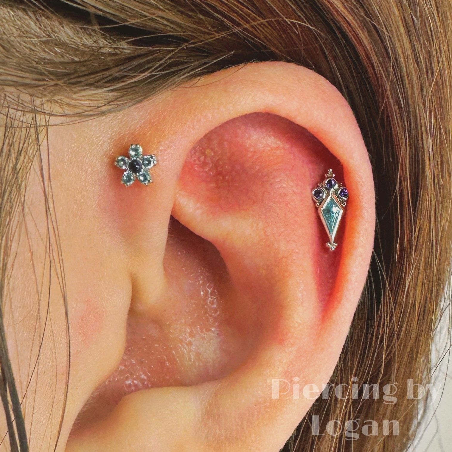 Close-up of ear with two decorative piercings: a flower stud and a teardrop-shaped piece with blue gems.