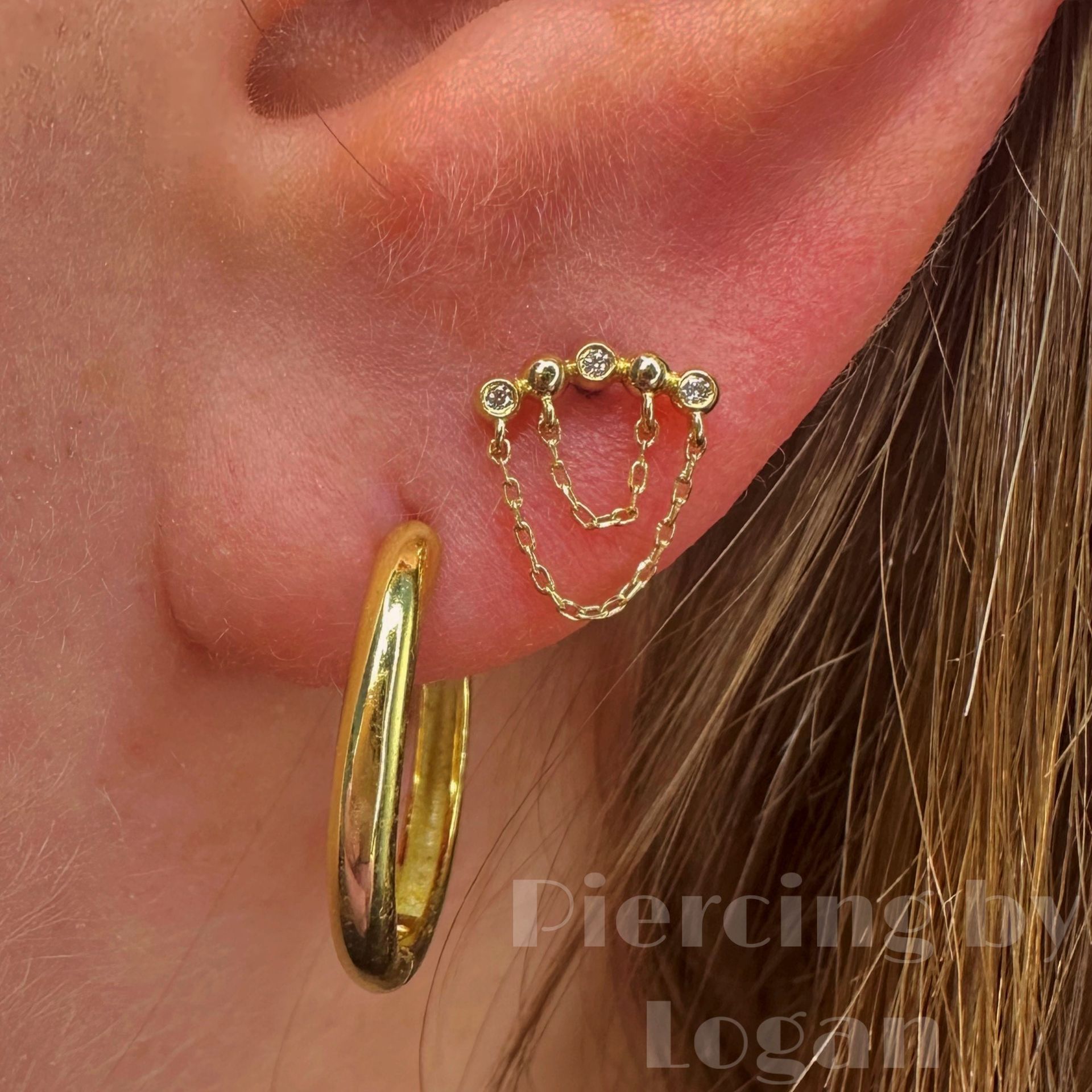 Gold earrings on a person's ear. One is a hoop, the other a bar with chain.