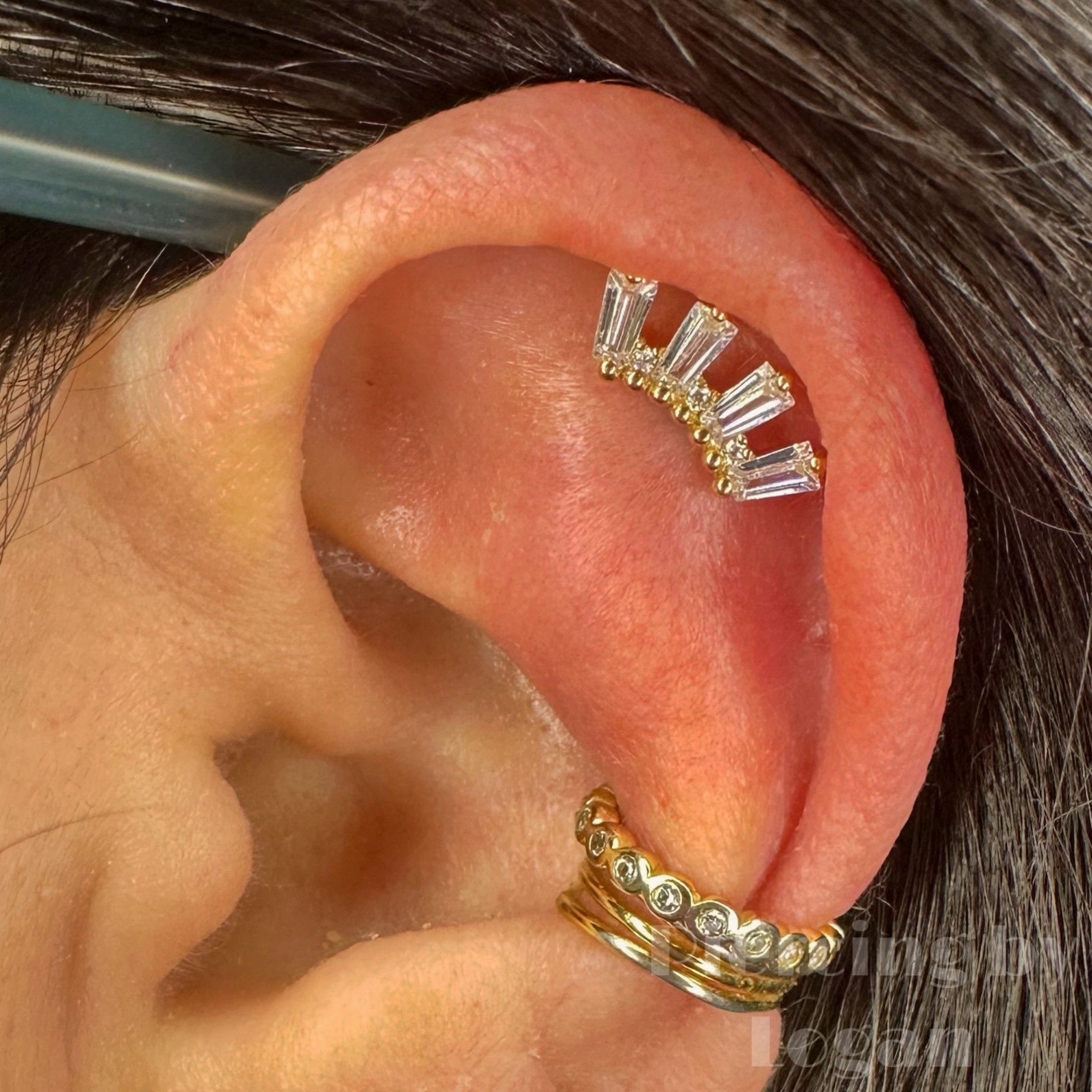 Ear with two gold earrings: a ring and a crown-shaped piercing with clear and gold stones.