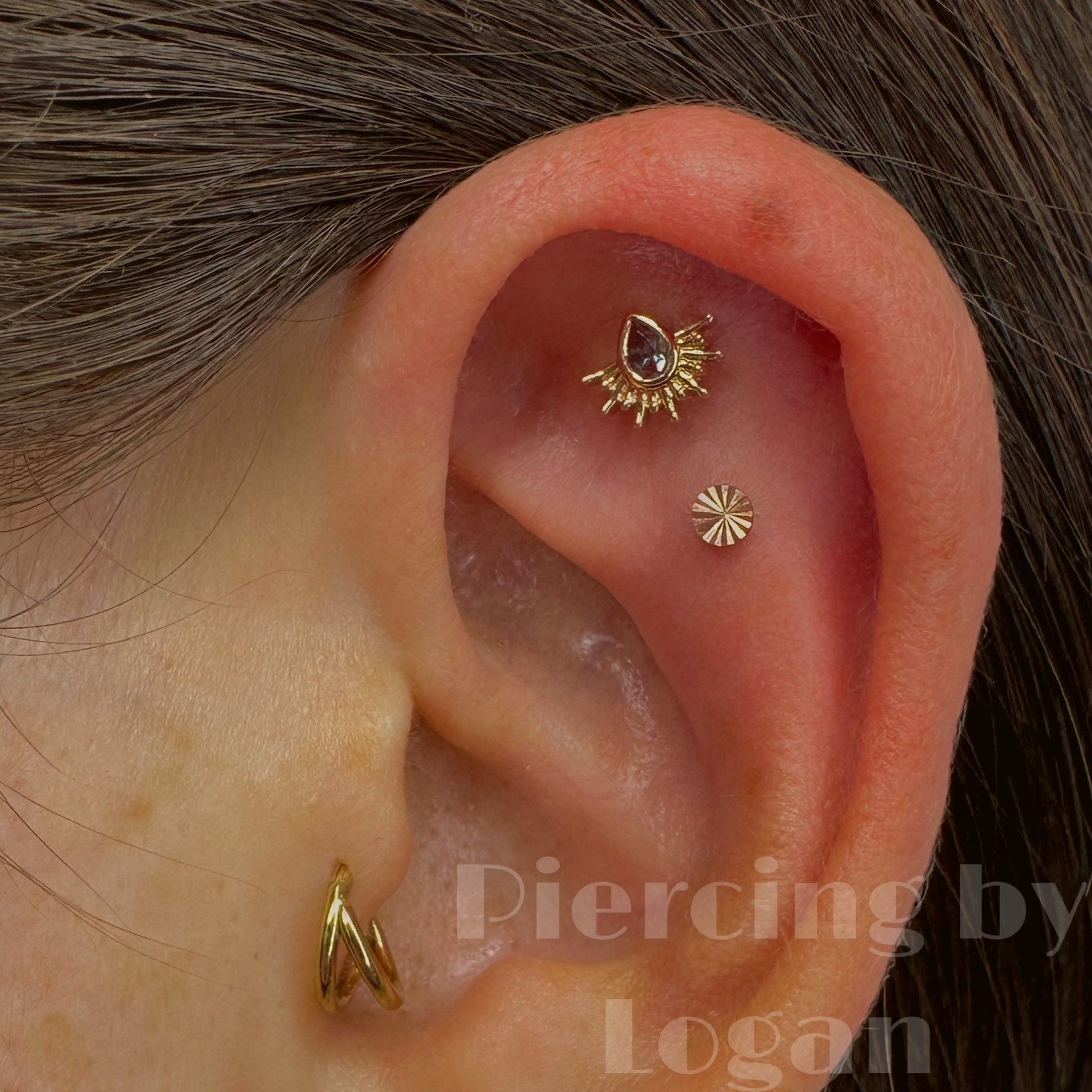 Ear with multiple piercings: conch, forward helix, and helix. Gold jewelry, tan skin.