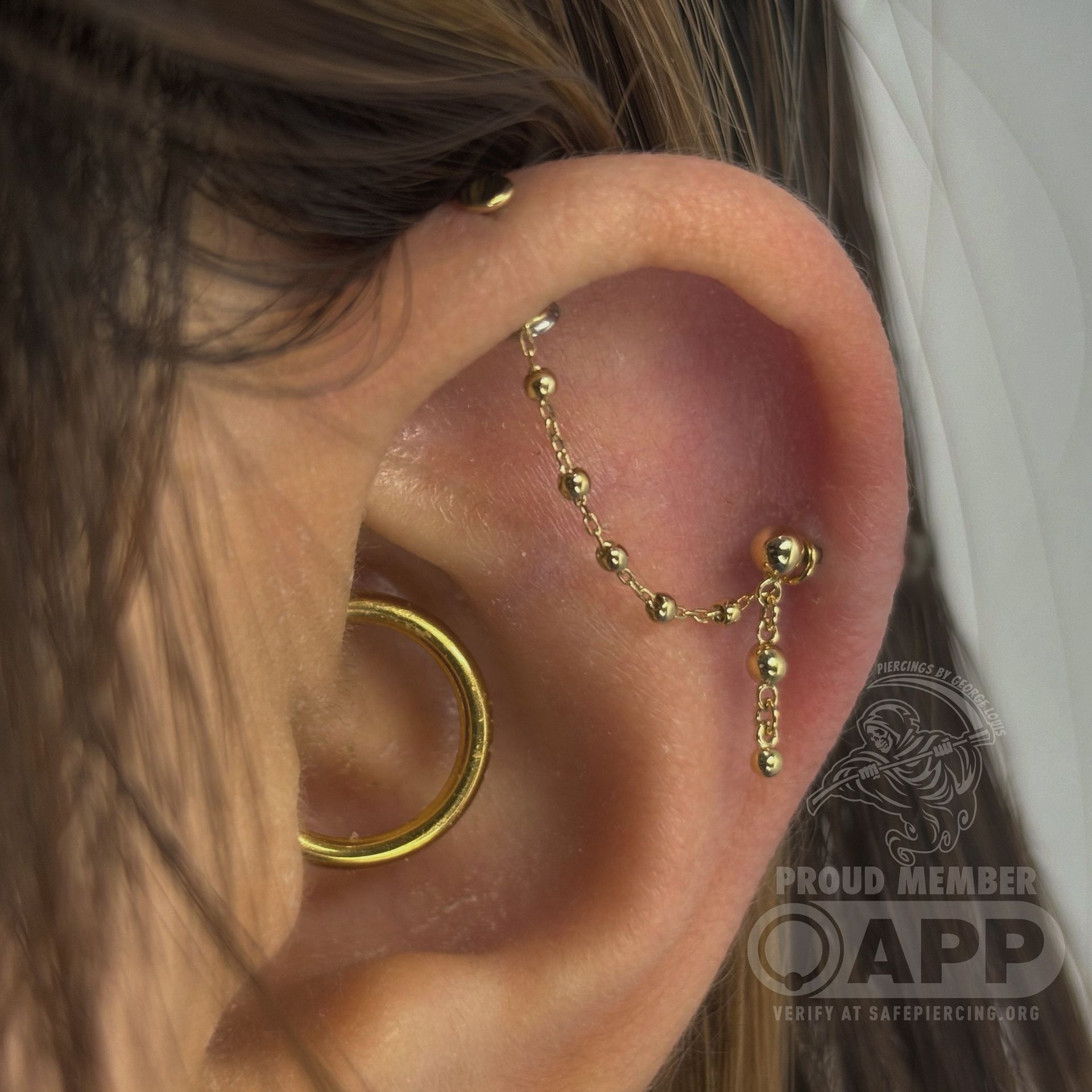 Ear with multiple gold piercings; chain connecting helix and conch.