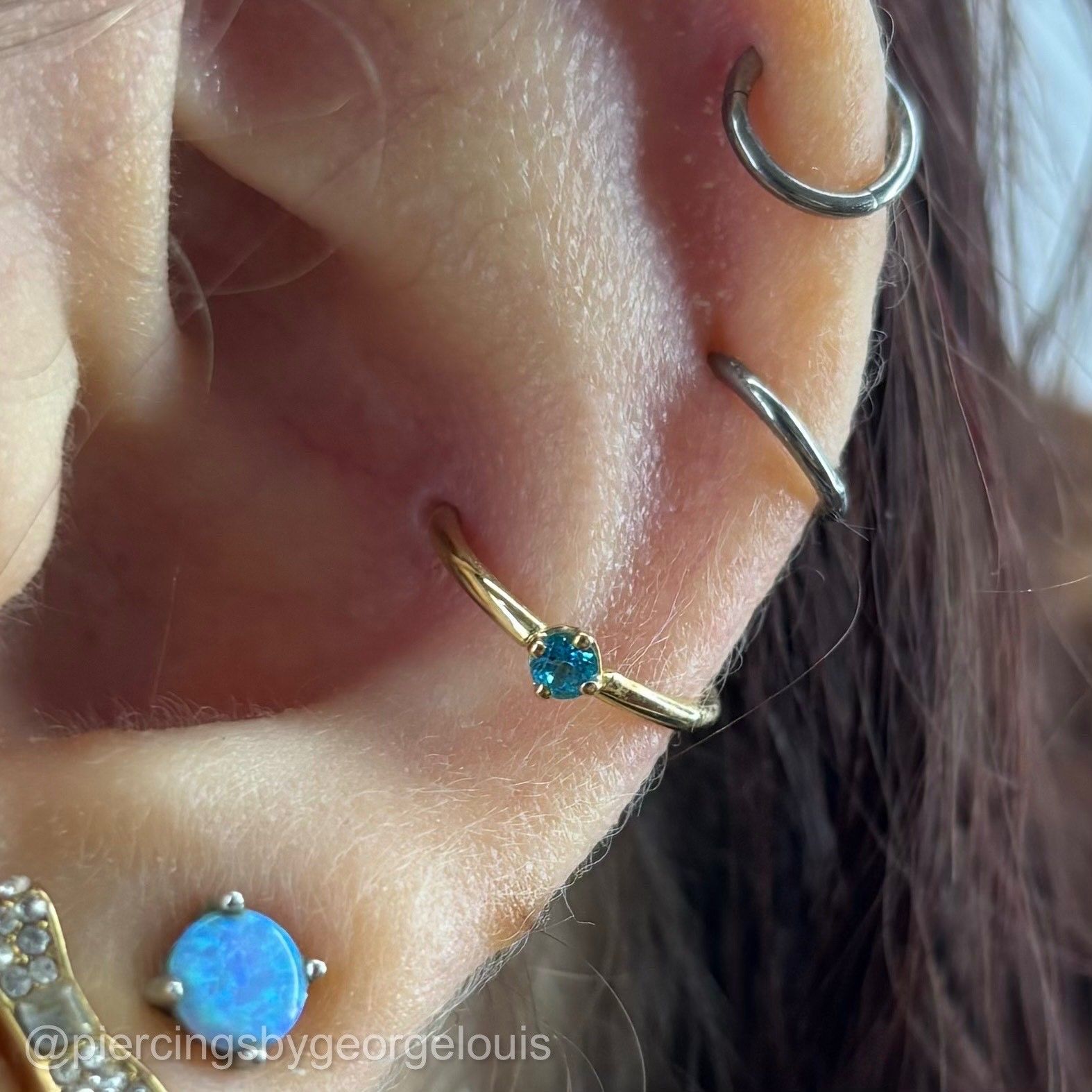 Close-up of ear with several piercings, including a gold hoop with a blue gem.