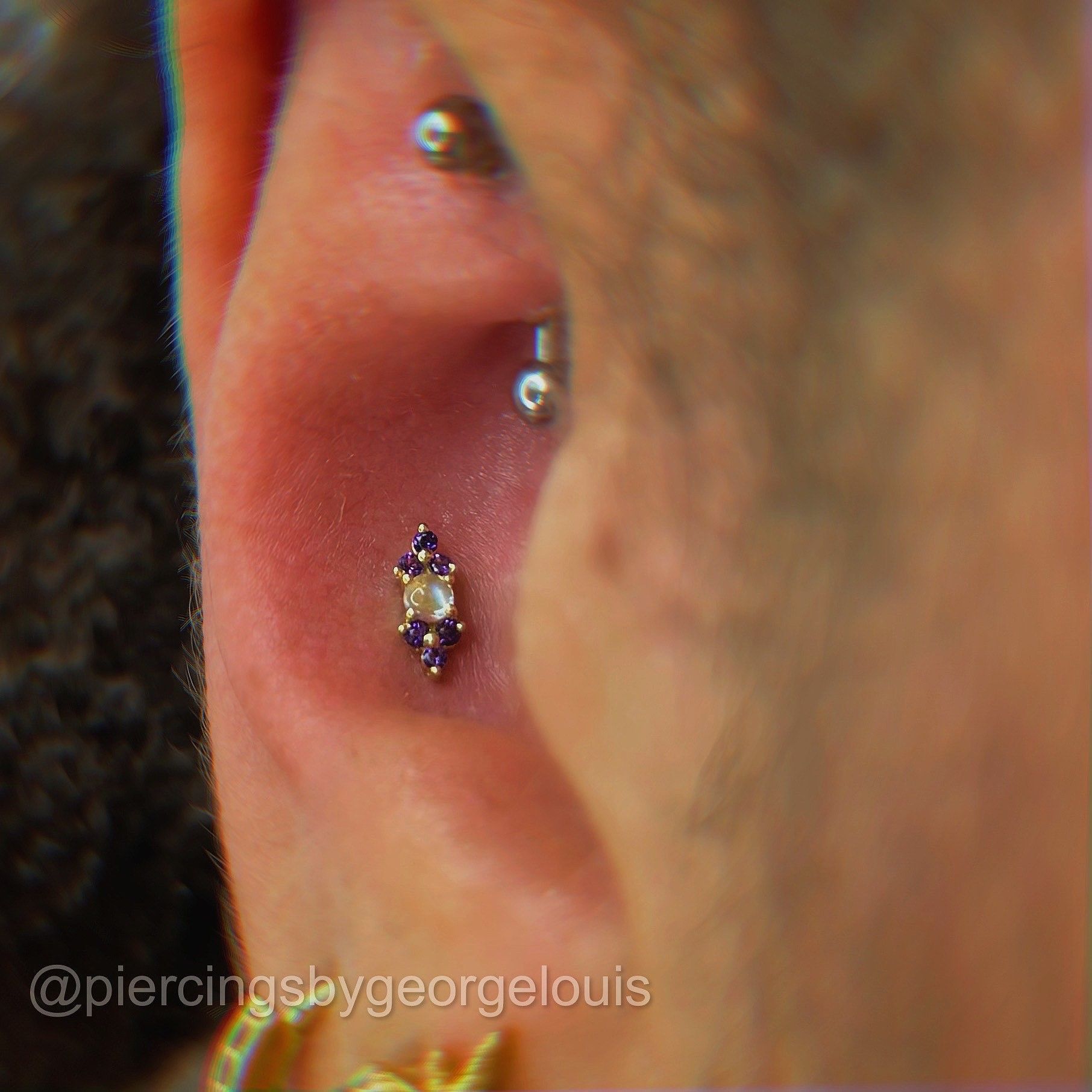 Close-up of an ear with multiple piercings, including a gold and purple gemstone stud.