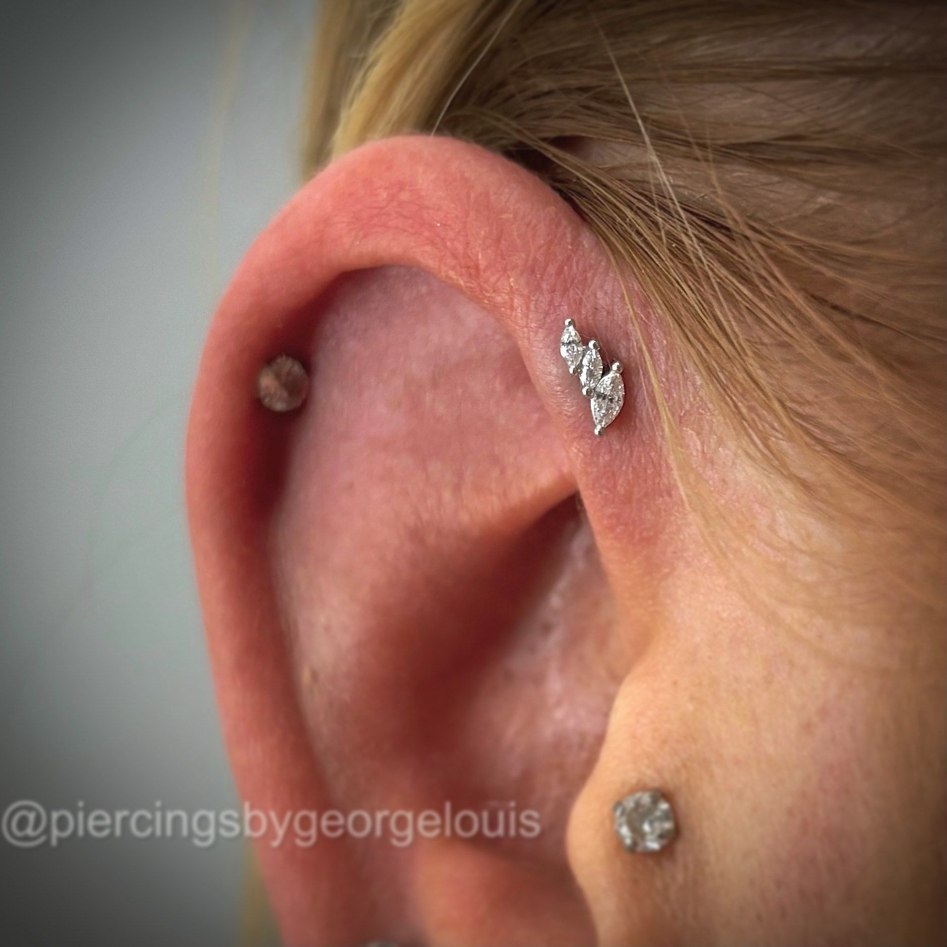 Close-up of an ear with three piercings. The ear has silver jewelry including a cluster design on the upper ear.
