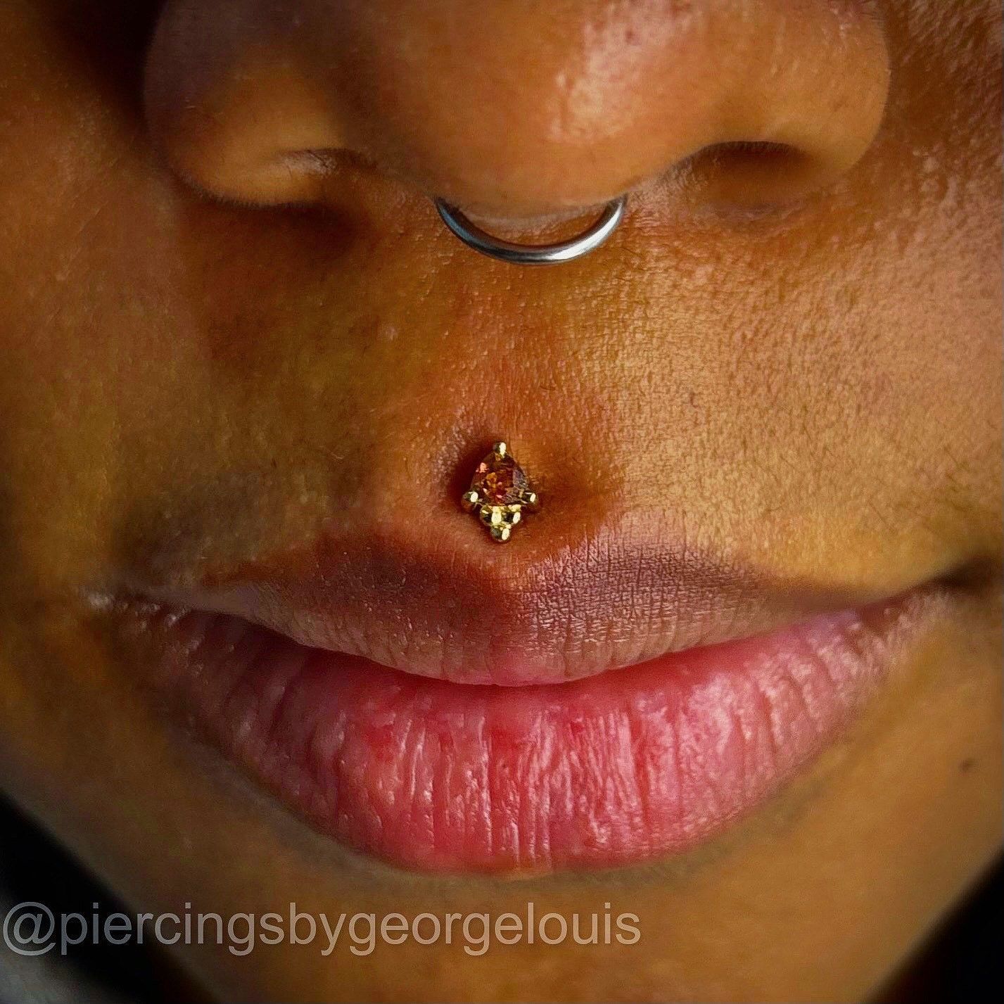 Close-up of a person's face featuring a philtrum piercing with a gold stud and an open septum piercing.