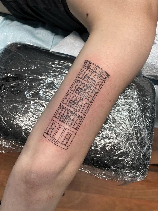 Tattoo of a tall building with windows on a forearm, fresh and wrapped in plastic.