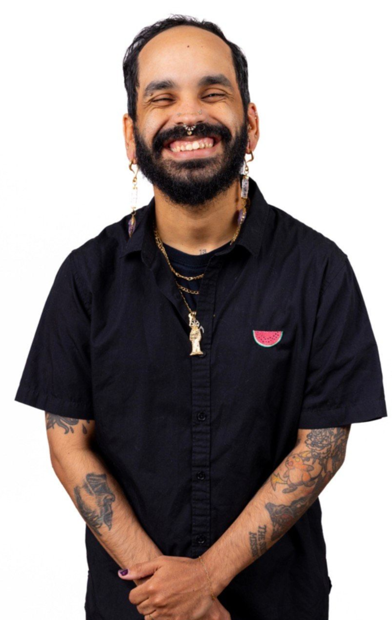 Person smiling, arms crossed, wearing a black shirt with tattoo sleeves, and nose ring.