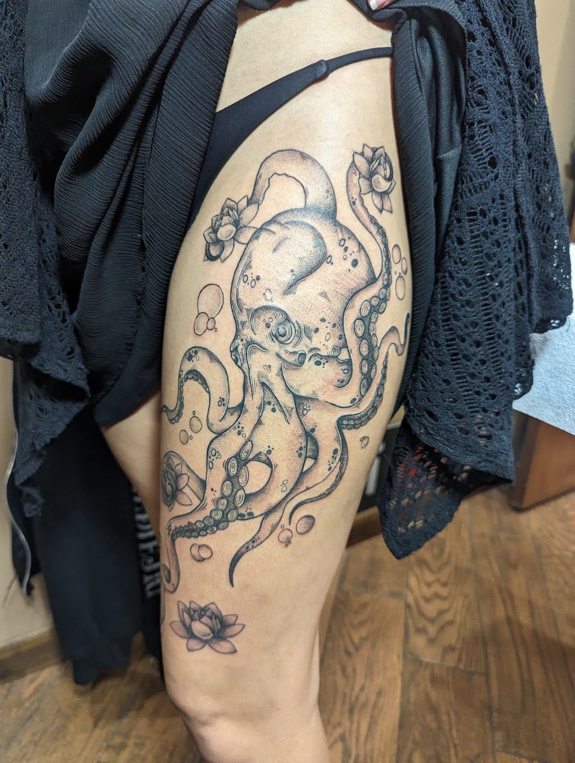 Tattoo of an octopus on a thigh, with lotus flower and bubbles; person wearing black clothing.