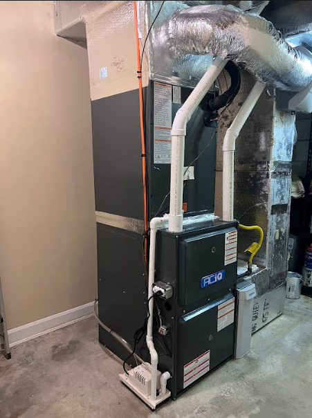 Furnace with exposed ductwork and white PVC pipes in a basement utility room.