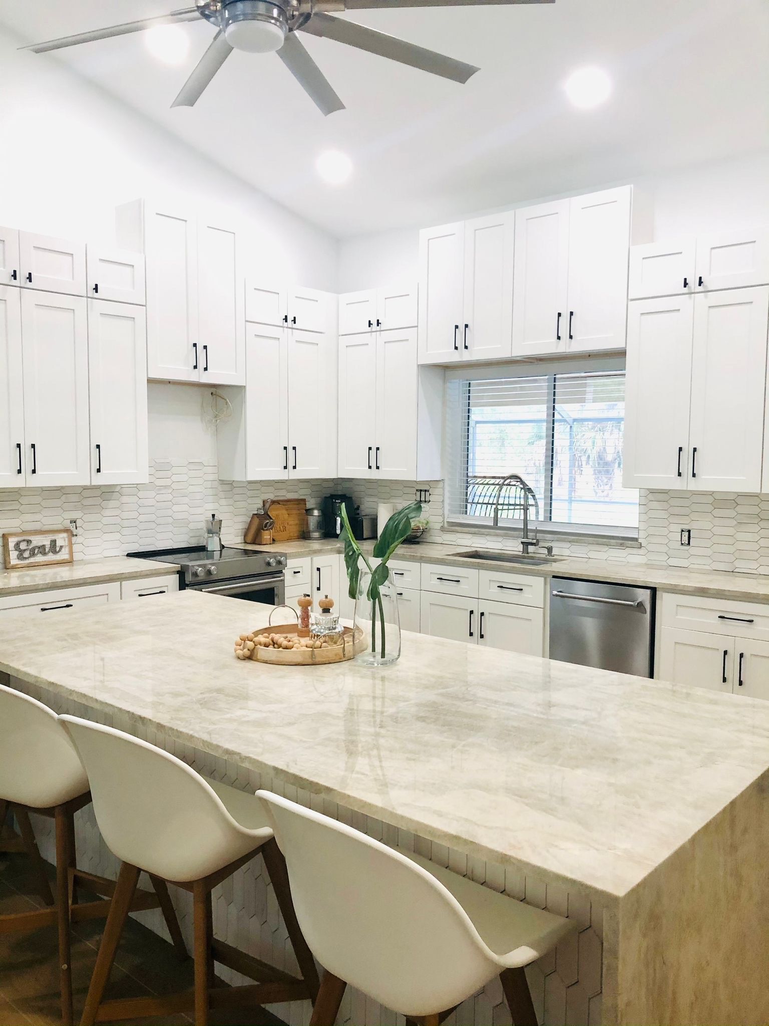 A Kitchen with White Cabinets , a Large Island , and A Ceiling Fan.