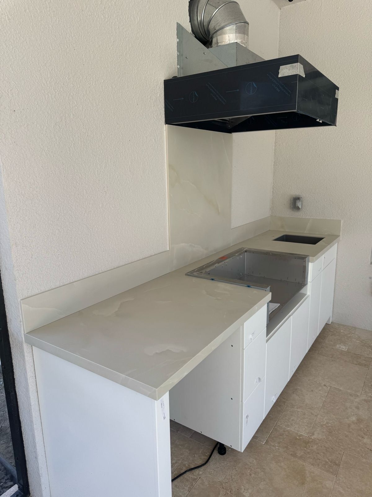 A kitchen with white cabinets and a hood above the sink.