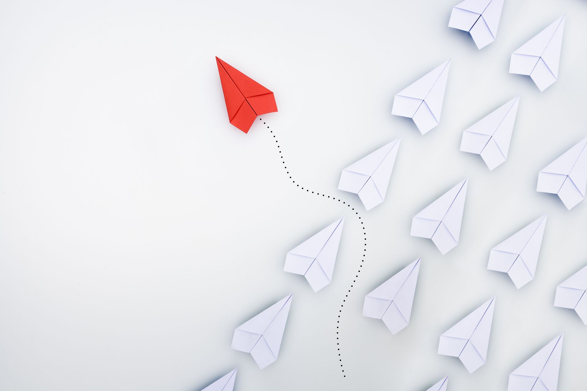 A red paper airplane is leading a row of white paper airplanes.