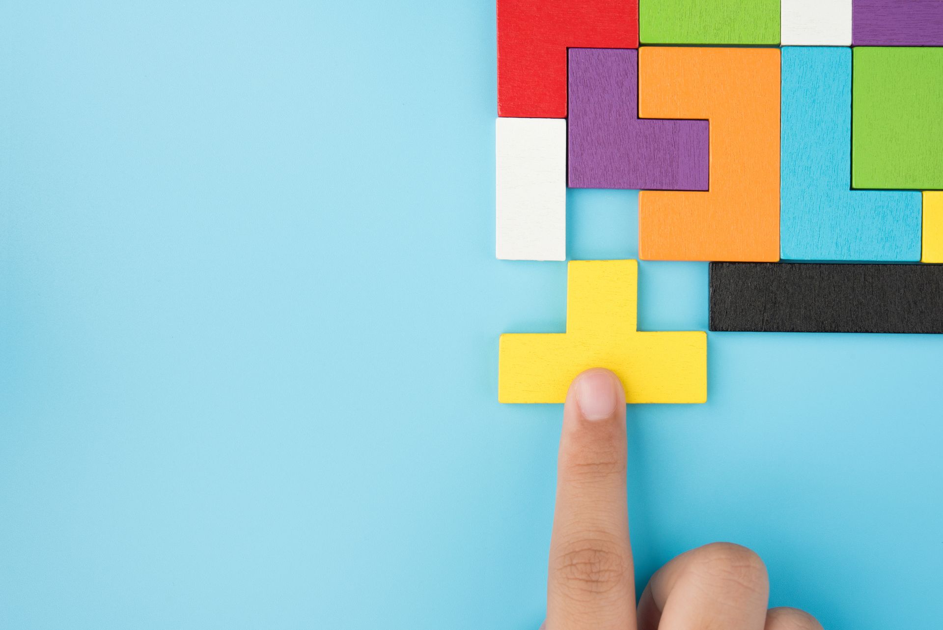 A person is pointing at a piece of a puzzle on a blue background.