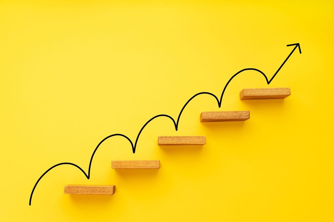 A wooden staircase with an arrow pointing up on a yellow background.