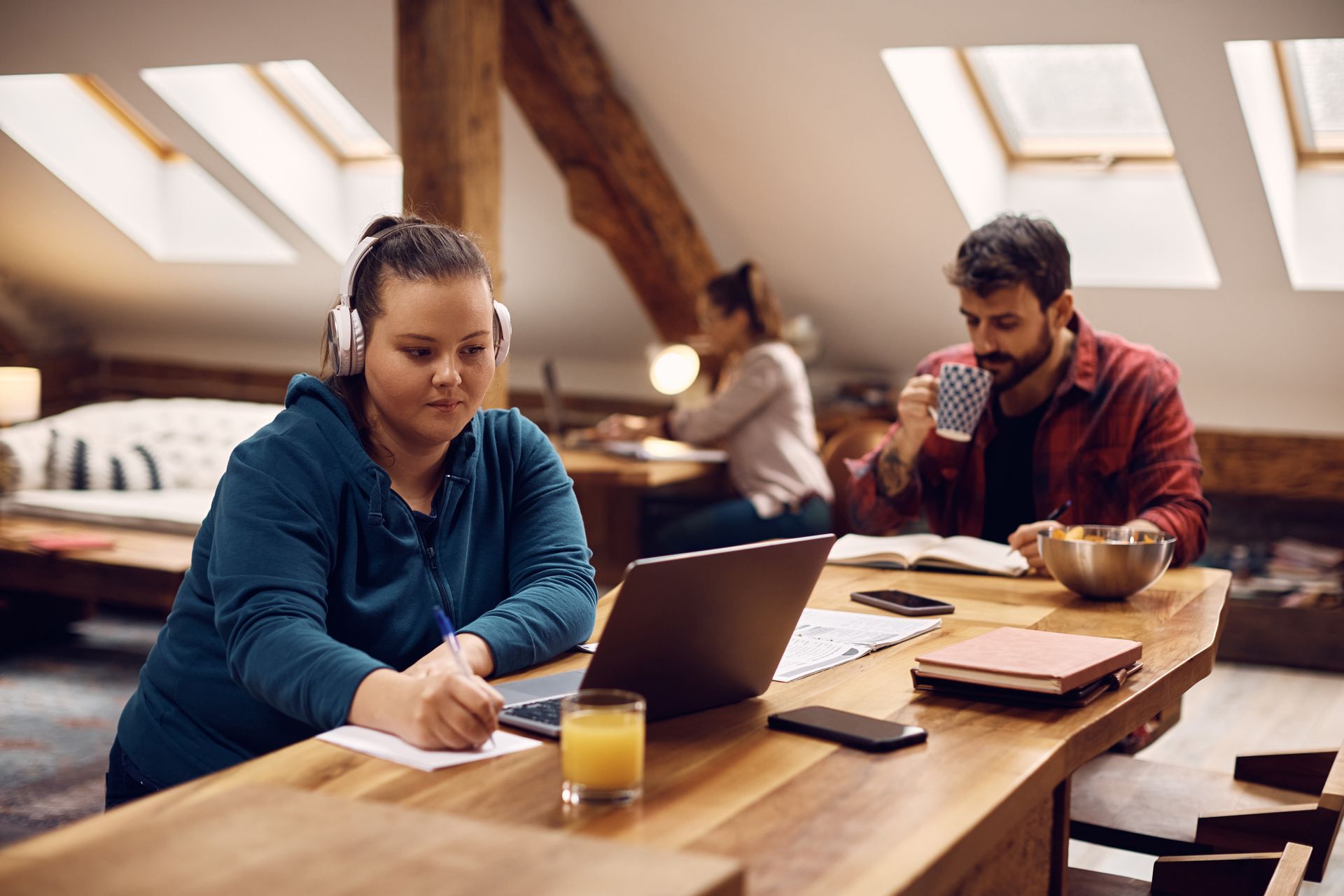 A woman is sitting at a table with a laptop and headphones on.