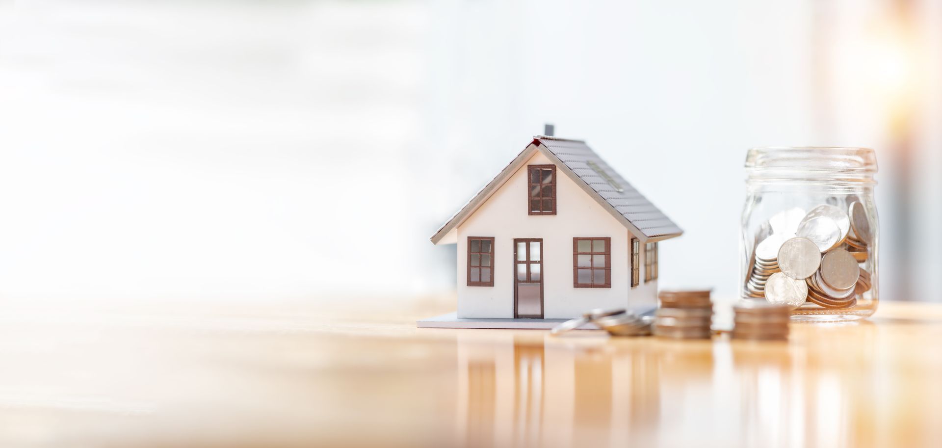 A model house sitting on top of a wooden table next to a jar of coins.
