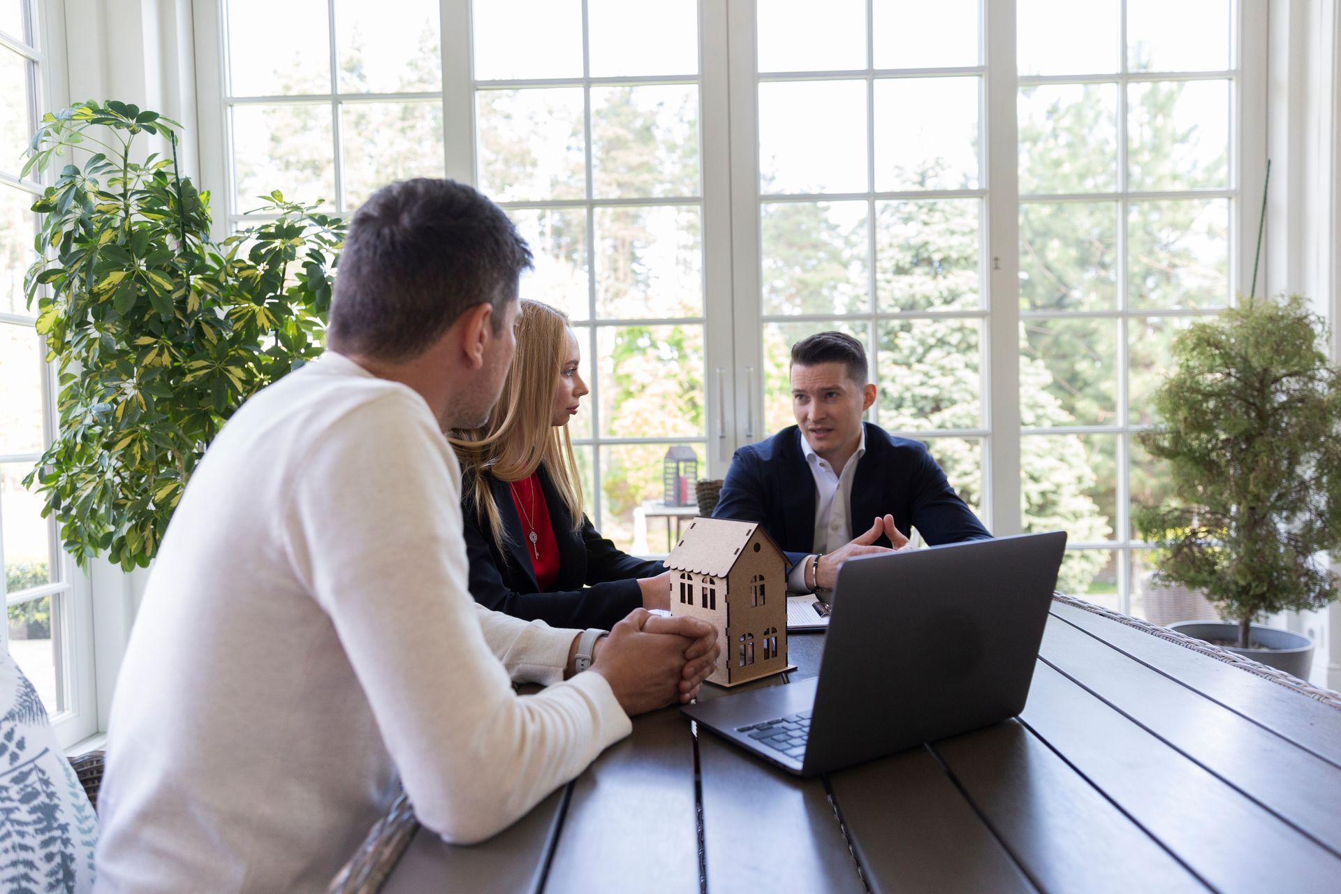 A group of people are sitting at a table with a laptop and a model house.
