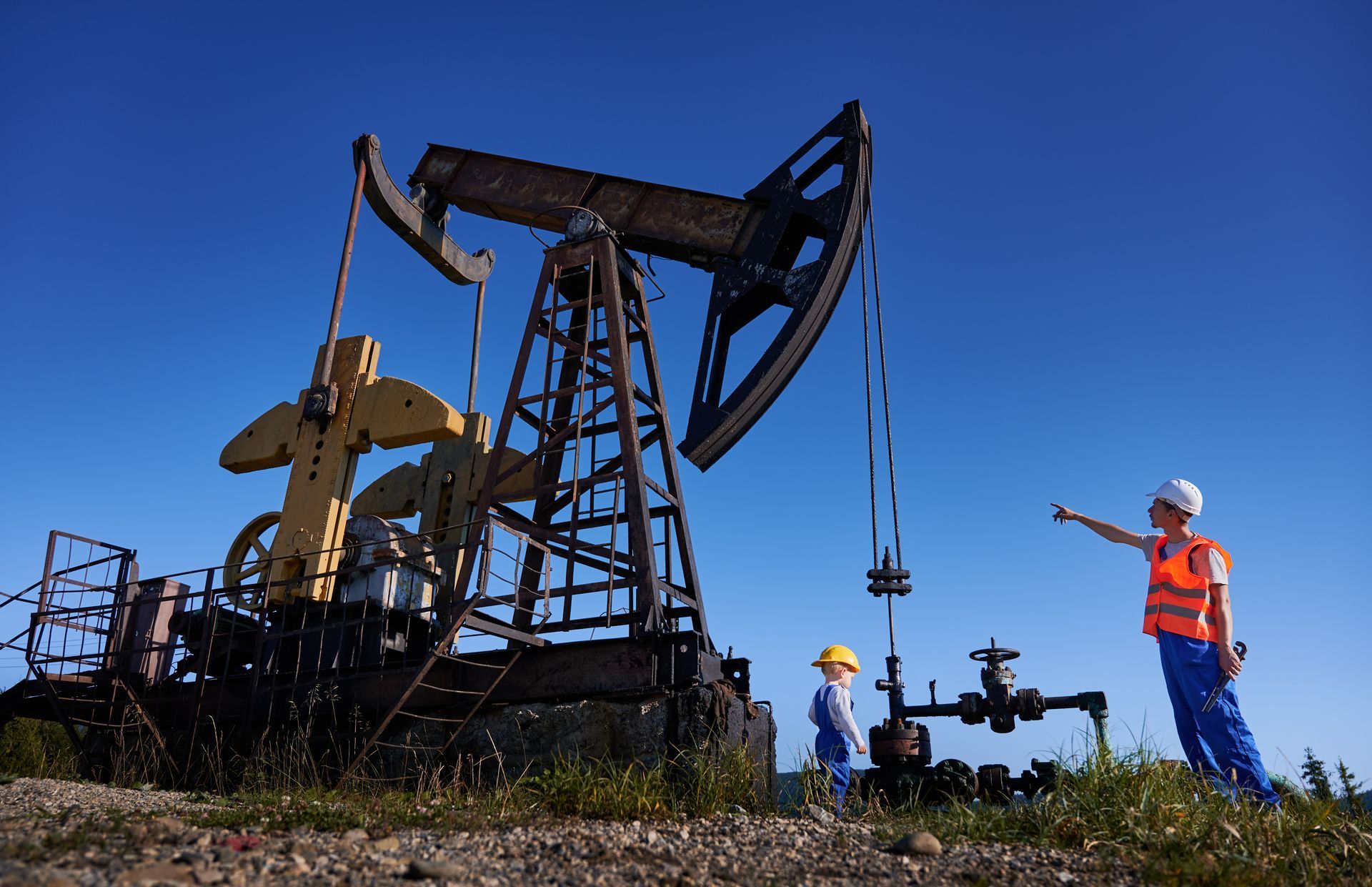 Oil pumpjack in a field with workers in safety vests under a clear blue sky Oil pumpjack in a field with workers in safety vests under a clear blue sky