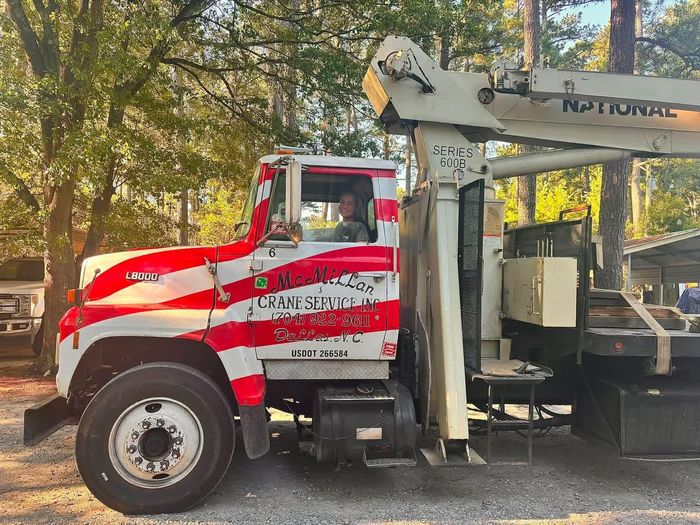 Red and white utility truck with a mounted crane parked among trees on a dirt roadside