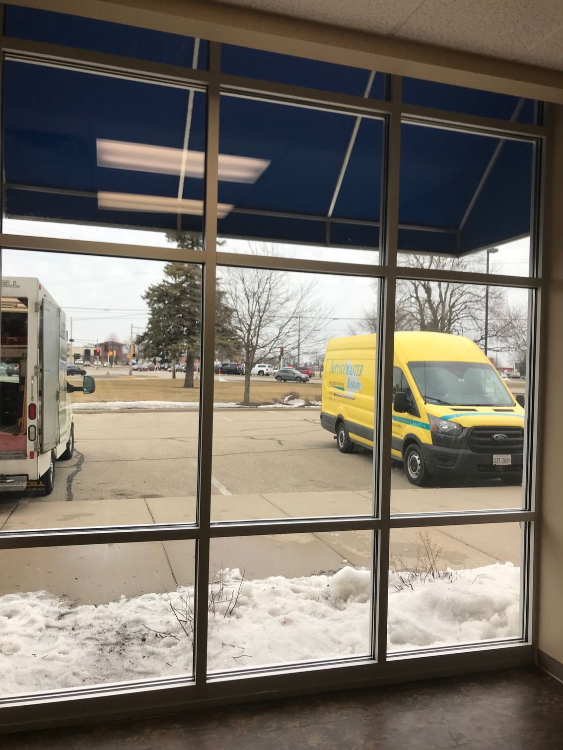 A yellow van is parked in front of a window with a blue awning.