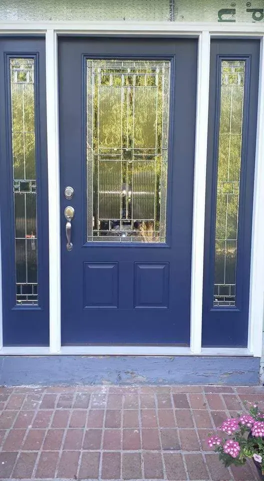Blue front door with sidelights, decorative glass, and brick walkway.