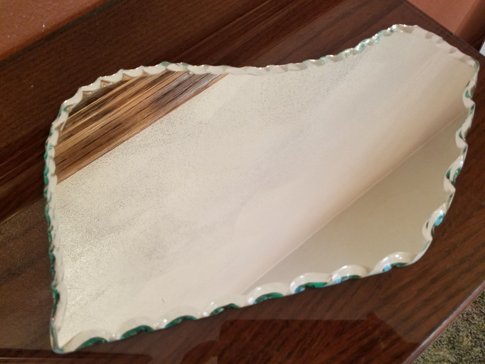 An irregular, wavy-edged decorative tray with a textured, off-white surface and a patch of natural wood grain at one end.