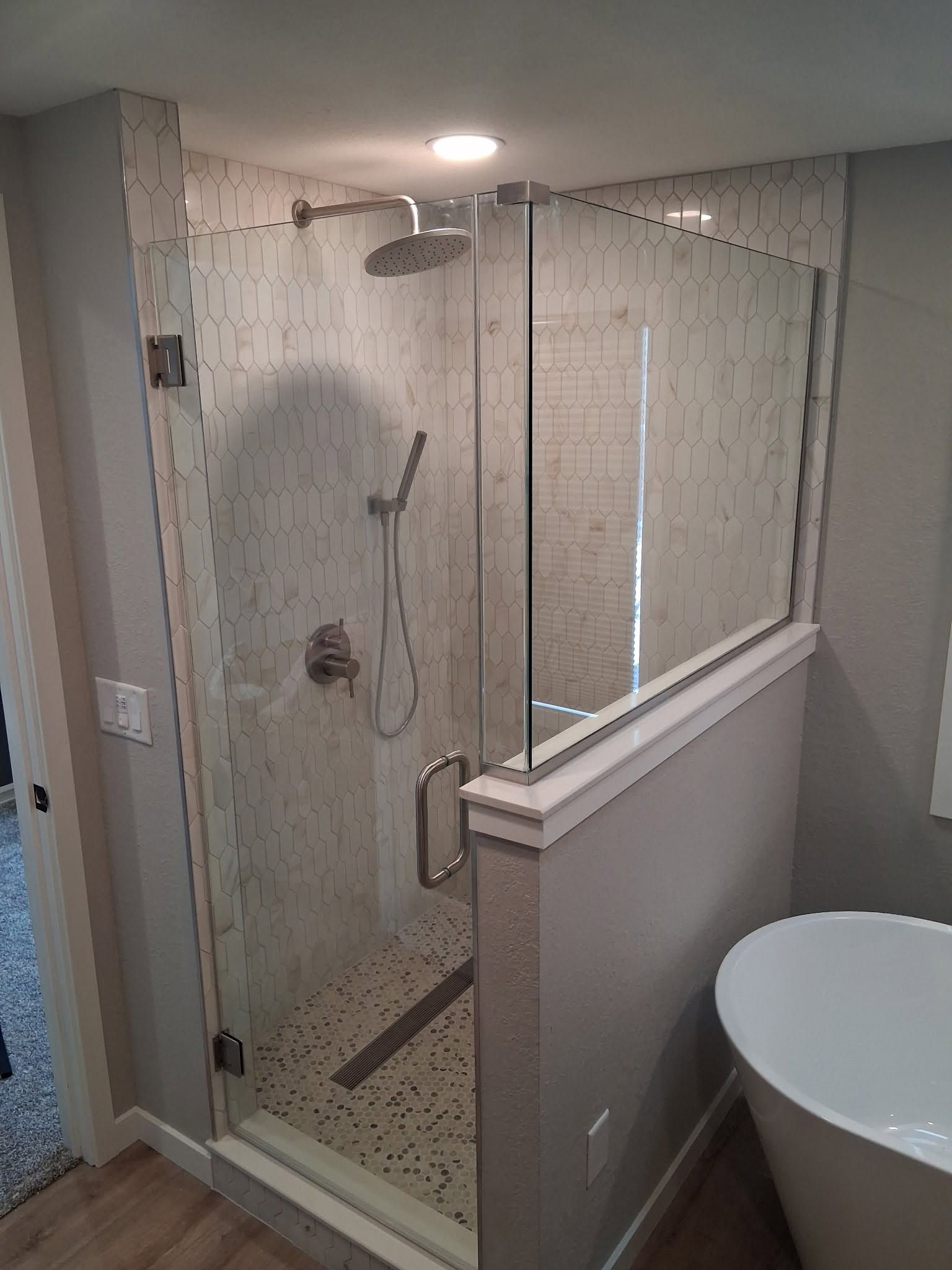 Custom frameless glass shower enclosure with brushed nickel hardware set on a tiled knee wall in a Rock County, WI bathroom